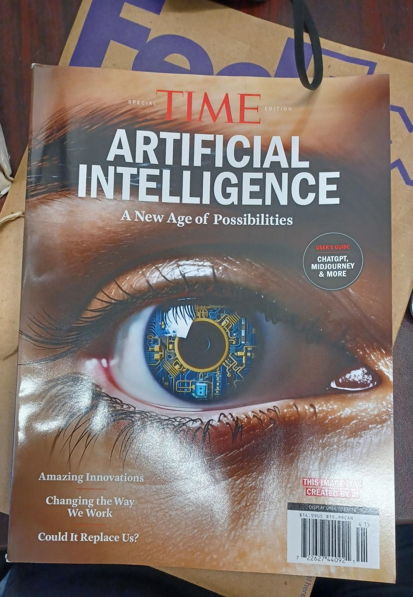 Picture of a magazine with title text reading "Time Special Edition: Artificial Intelligence: A New Age Of Possibilities," an several topic headlines, all over top of an "AI"-generated image of human eyebrow and eye, and the eye has a circuit board for an iris; a fedex envelope and desk are visible beneath the magazine