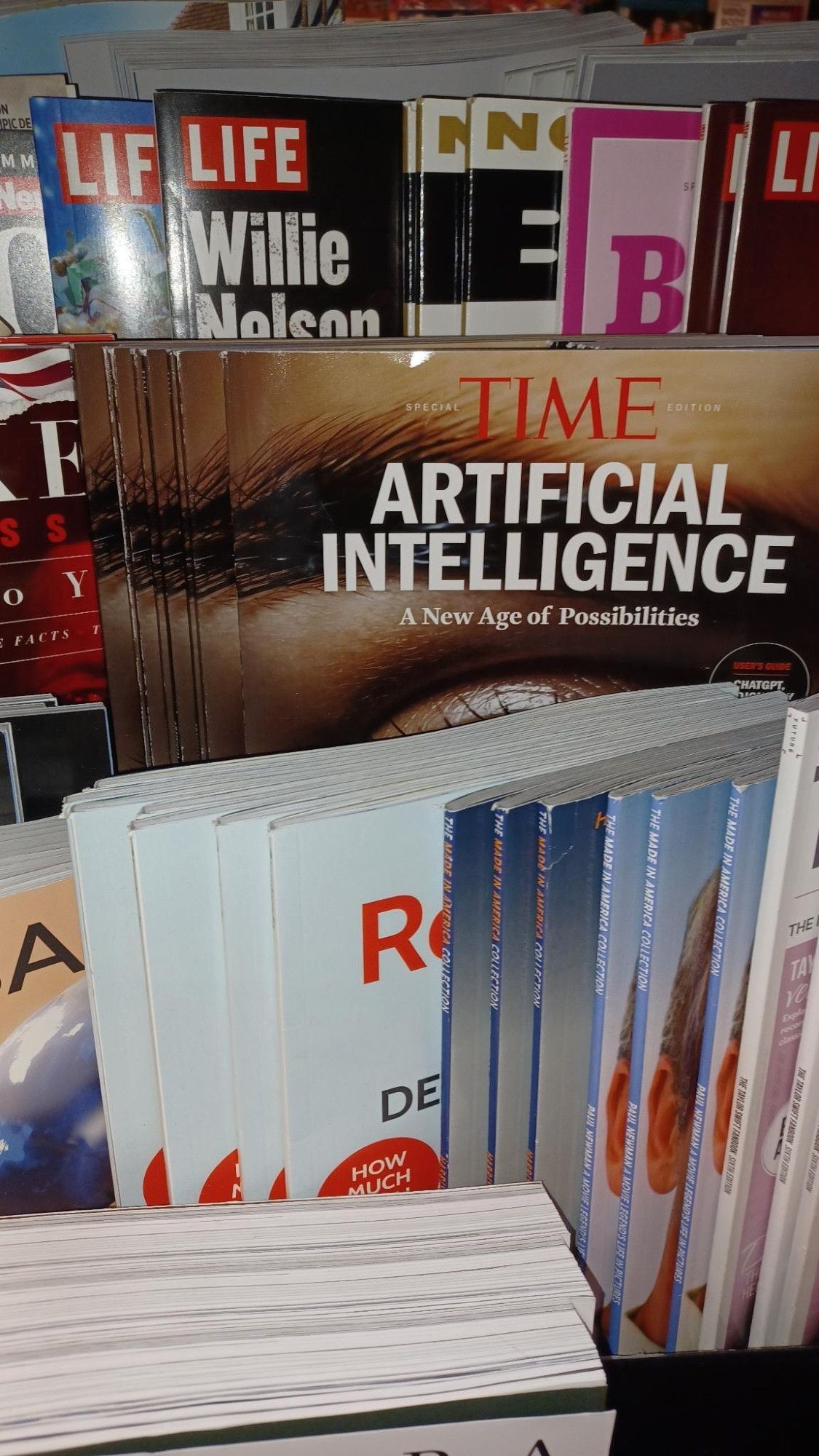 Picture of a magazine shelf at a bookstore filled with several different magazines but centered on one reading "Time Special Edition: Artificial Intelligence: A New Age Of Possibilities," over an "AI"-generated image of human eyebrow and eye