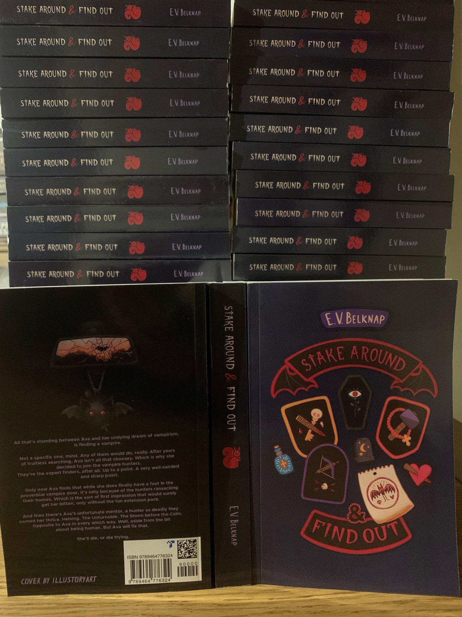 A big stack of author copies of my book, Stake around and find out. The cover depicts lots of vampire themed patches, on a purple denim background. The title is in patches too, with bat wings on the side. There’s a coffin with an eye-plant, a crossbow with a garlic pierced by two arrows, a stake crossed with a skeleton key complete with skull, a hammer with a rosary, a staked heart, a tombstone with a crescent moon, and a paper drawing of a bat, kid style, with a heart and skull added. The spine has a red squirrel. The back has a bat plushie dangling from a cracked rear view mirror, the plushie stabbed through with a mini stake, along with the blurb