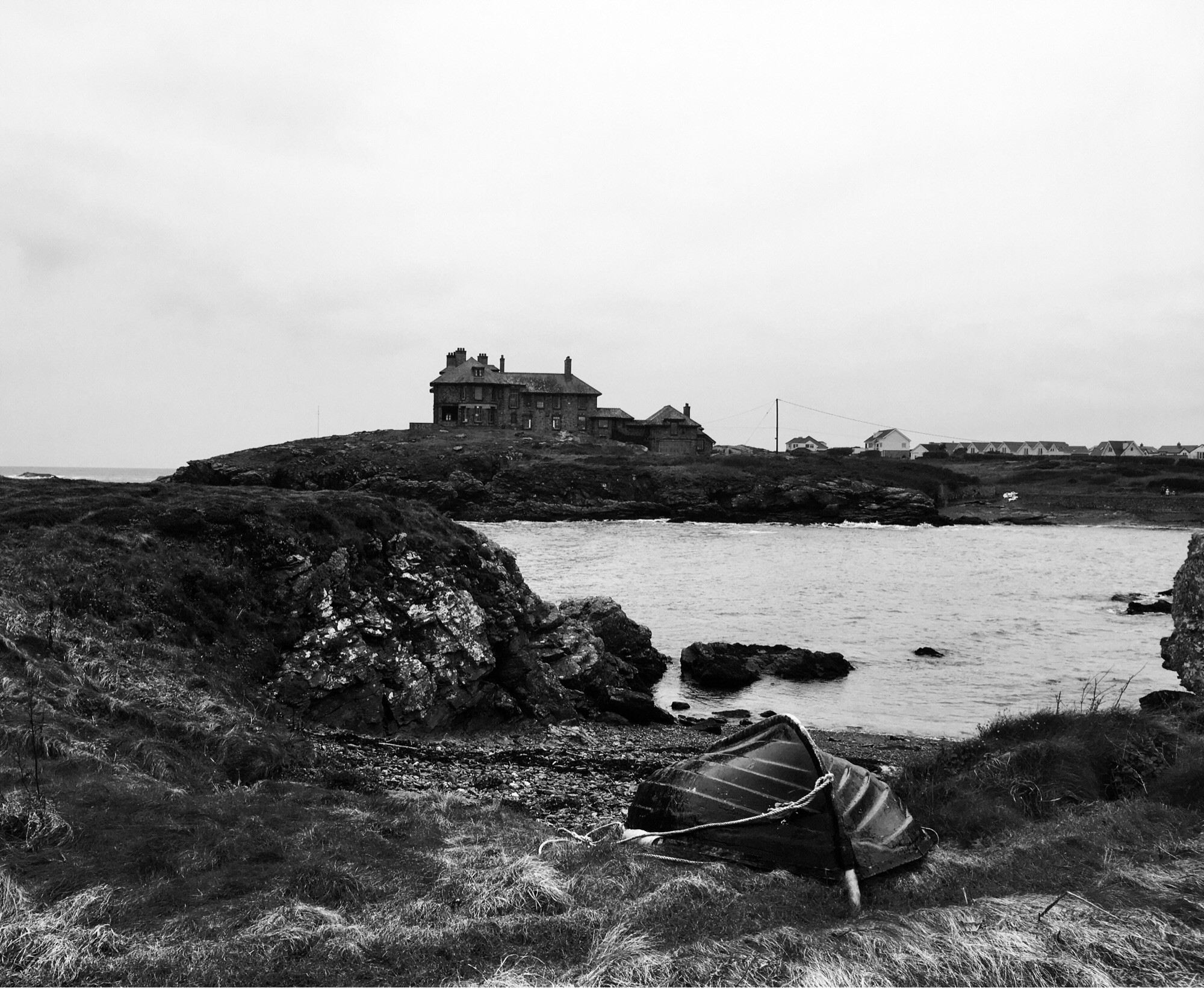 A house that is definitely not haunted sits on a headland overlooking a small beach with an overturned rowing boat lying on shingle above the high tide strandline.