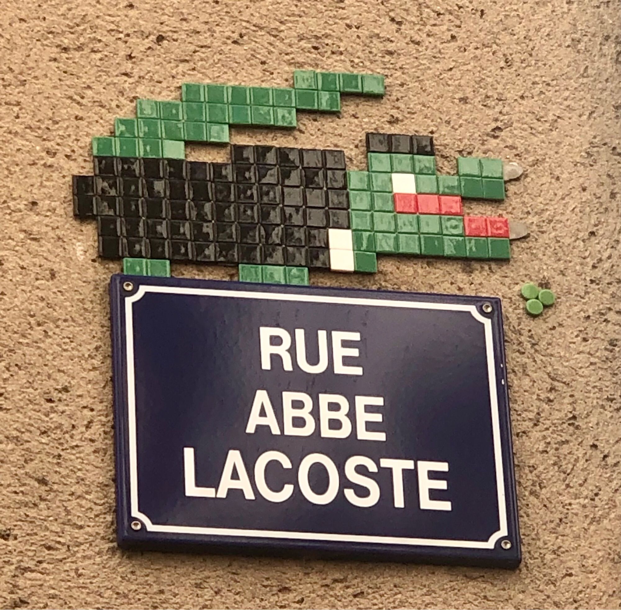 Au-dessus de la la plaque de la rue Abbé Lacoste, une mosaïque représentant de crocodile Lacoste avec une tenue d’abbé