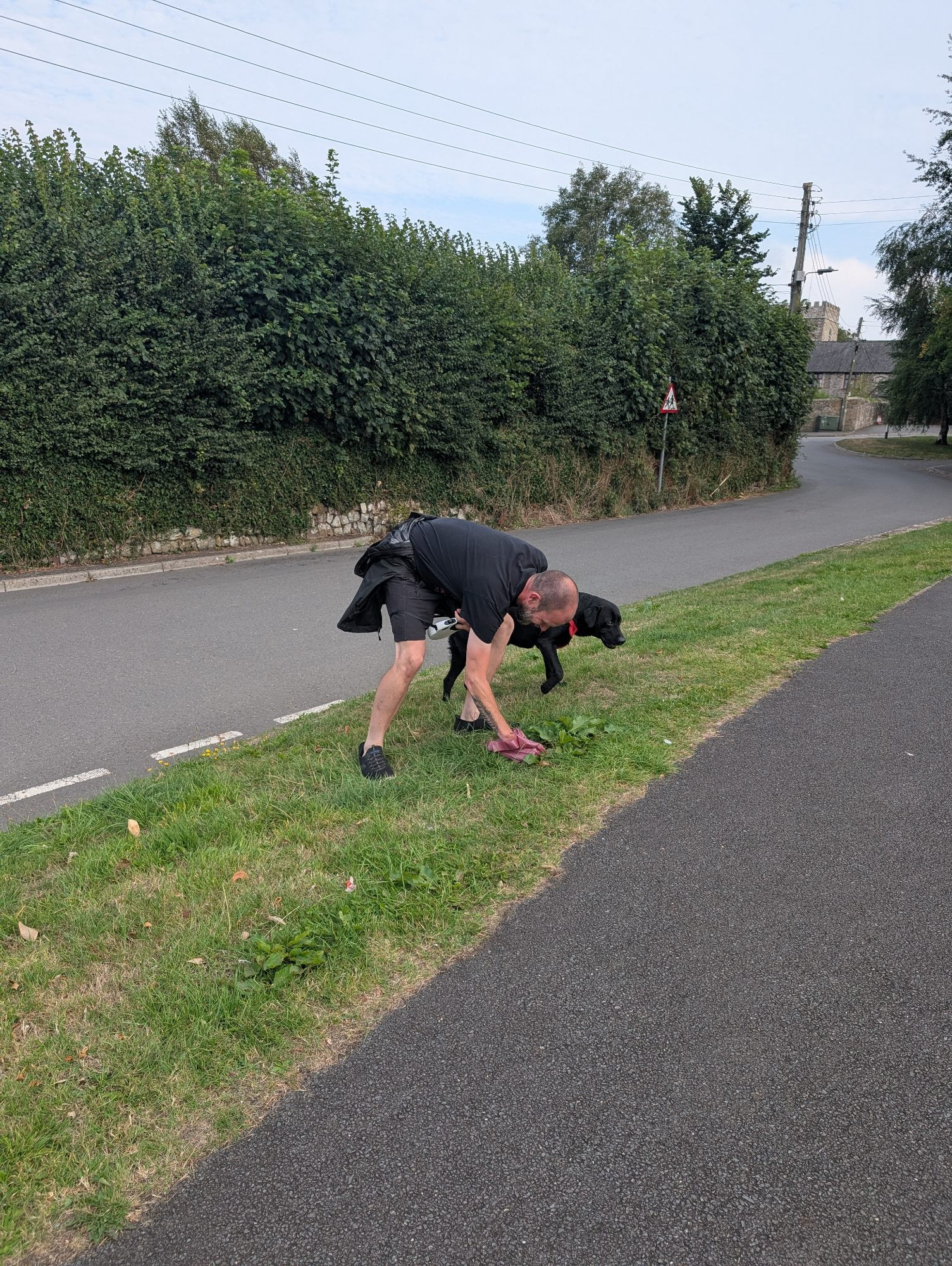 A man picking dog shit up from the side of a road. Again. 