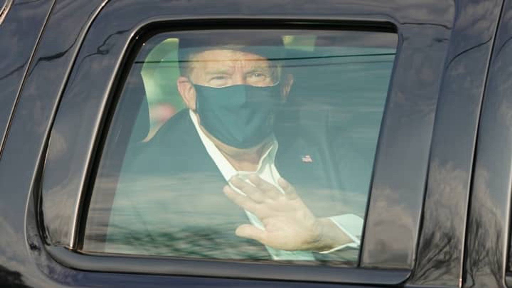 Trump wearing a black facemask waving from his car