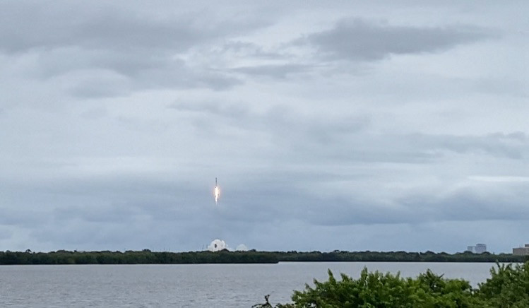 View of a rocket launching from a vantage point across a body of water.