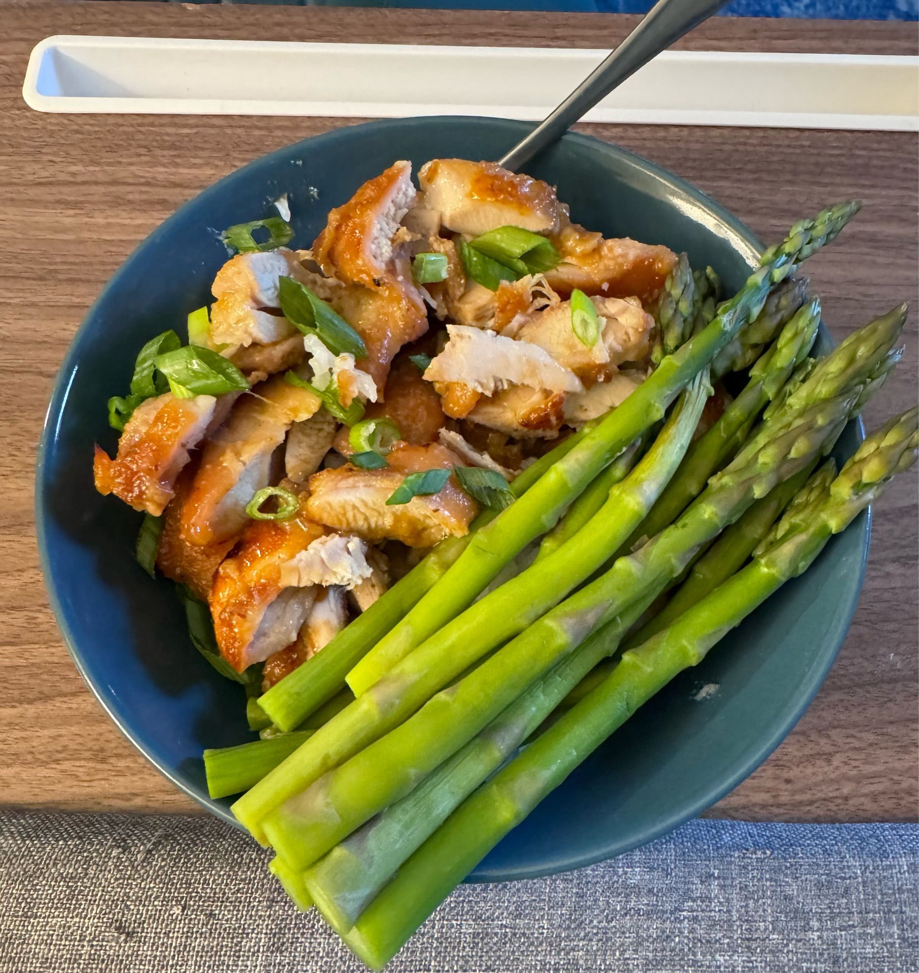 Oven baked chicken thighs with asparagus and rice in a blue bowl.