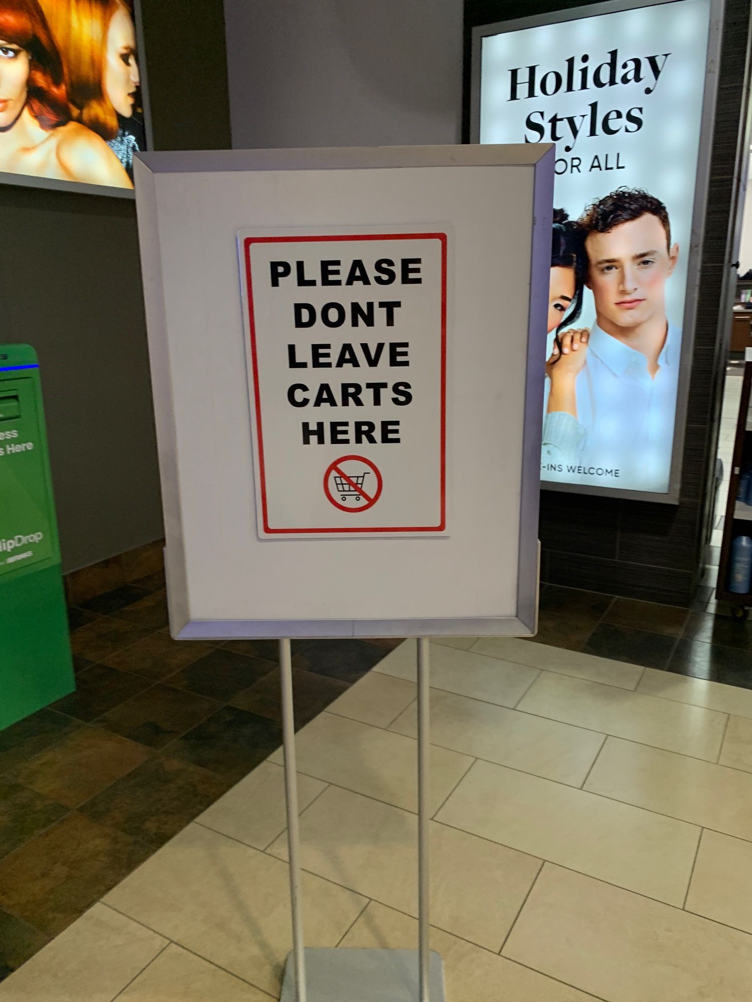 A sign in a mall that says “please don’t leave carts here” with the apostrophe missing from “don’t”. Below the message is an icon of a shopping cart in a red circle with a slash through it.