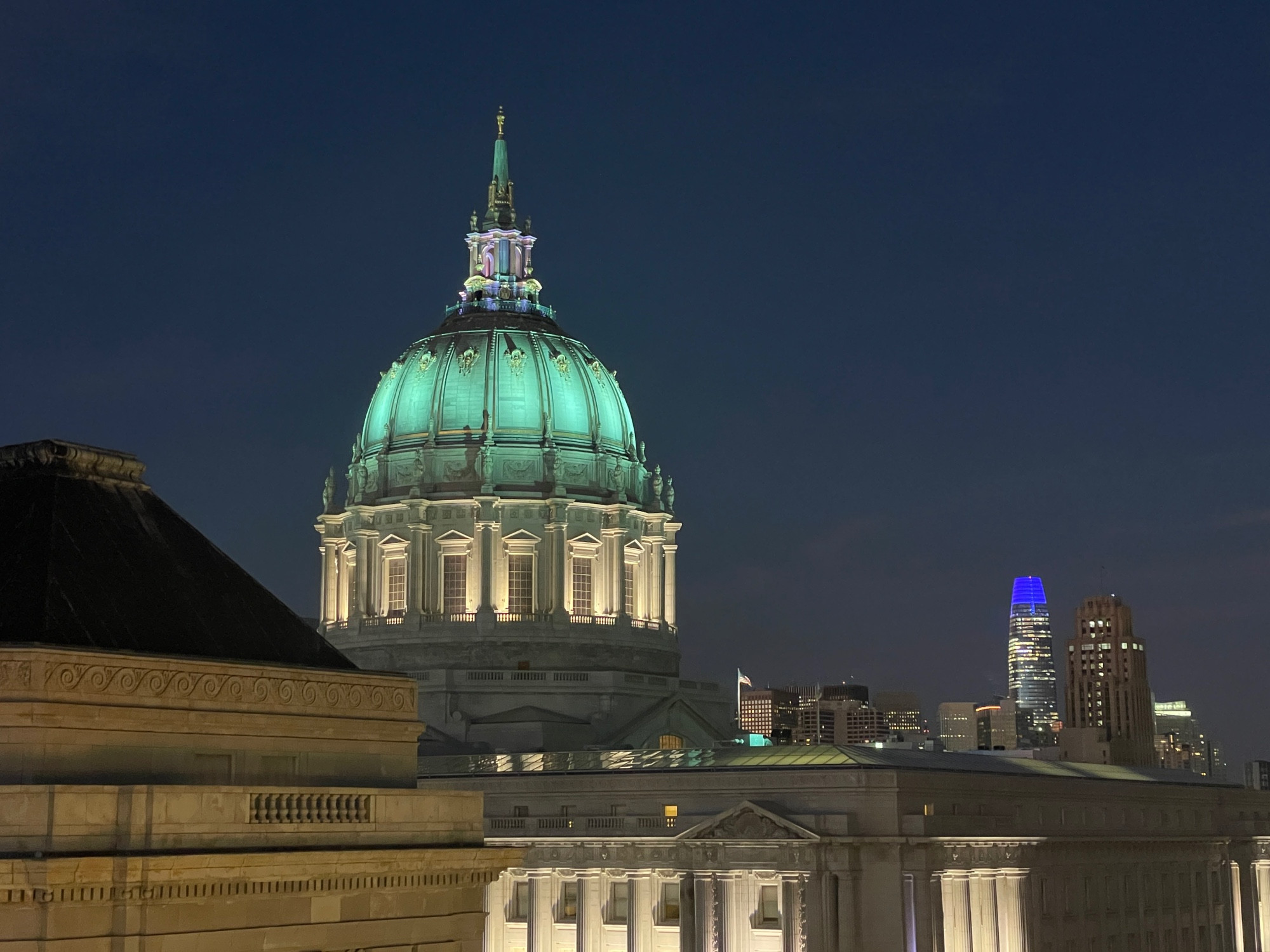 SF City Hall as seen from the top of Davies Symphony Hall. Its dome is illuminated in light green. The top of the Salesforce Tower is also visible