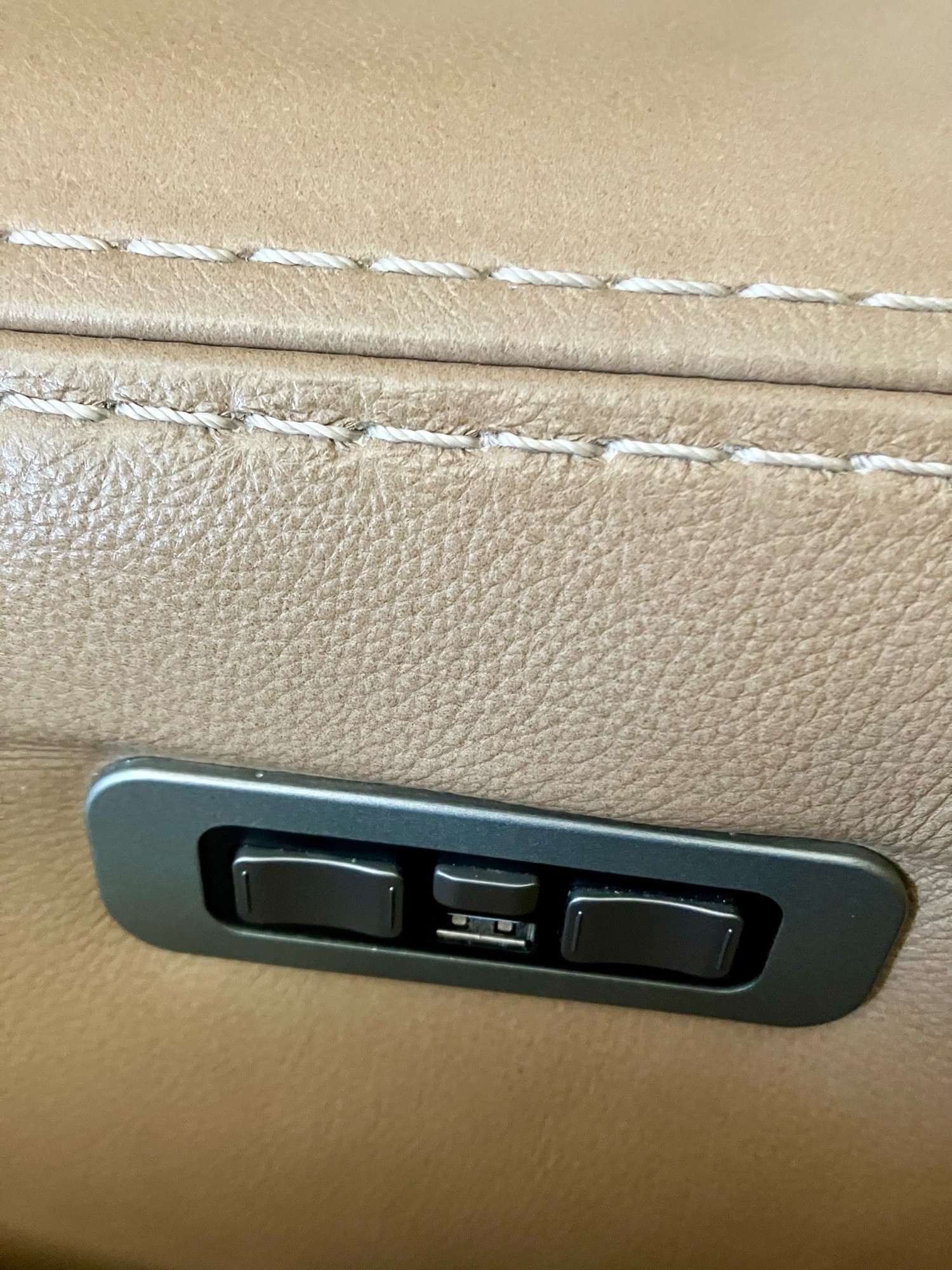 A well used tan couch armrest with reclining buttons and a USB (old style) charger port.