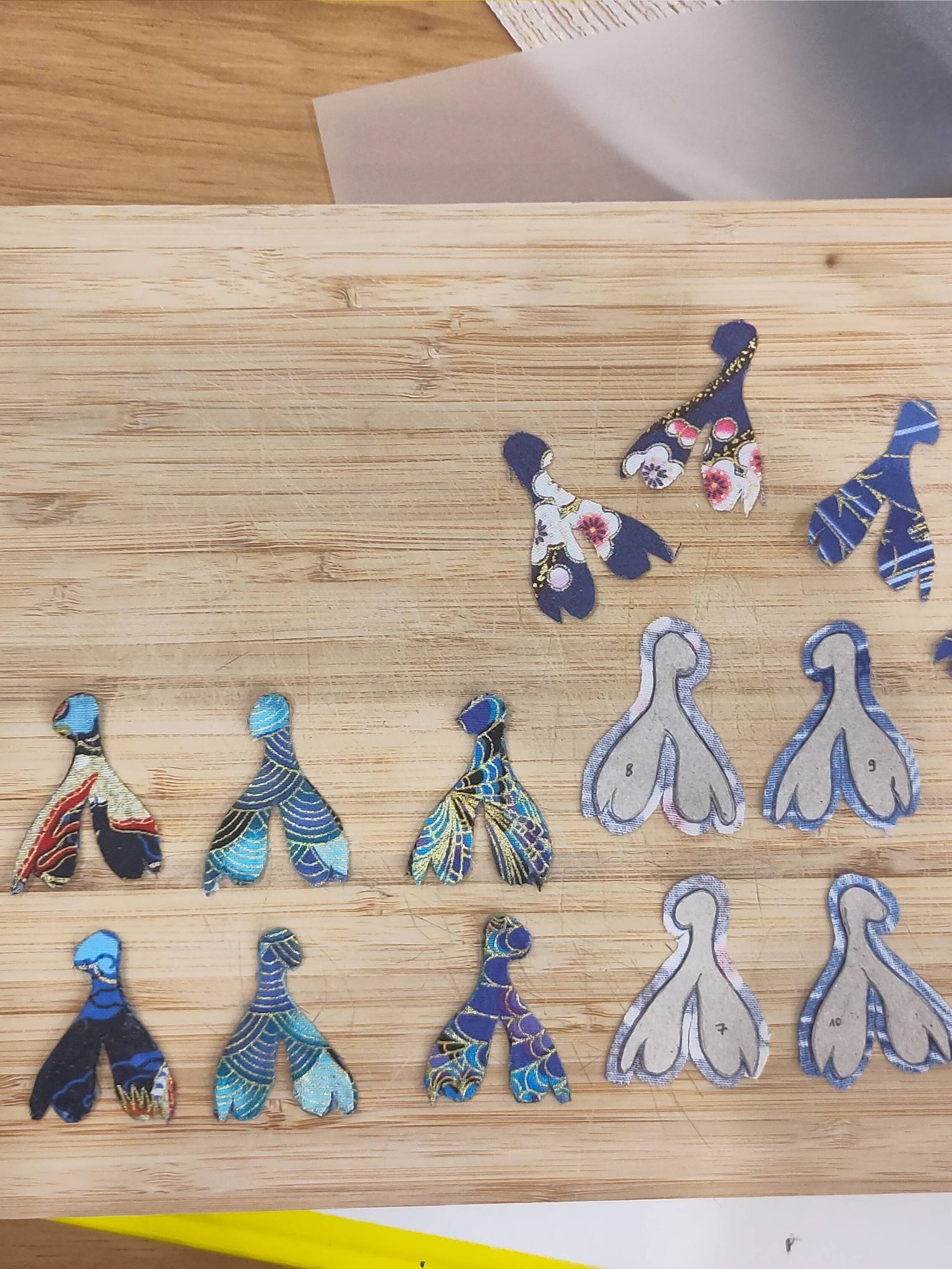 Boucles d'oreilles découpées dans du carton en forme de clitoris avec du tissu collé dessus. Le tissu est à motifs dans des teintes de bleu.