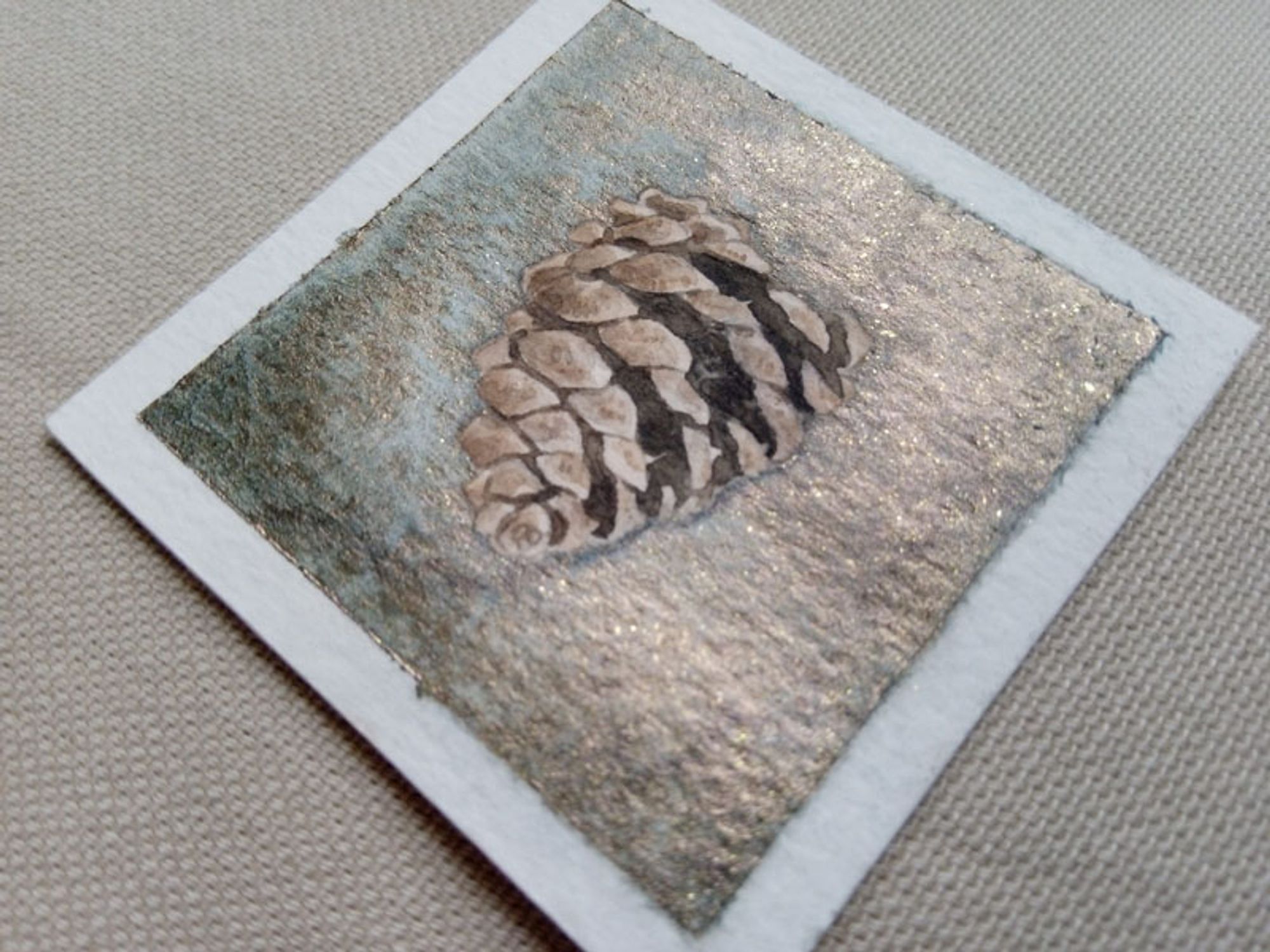 small watercolor painting of a pinecone on a shiny green/gold background.