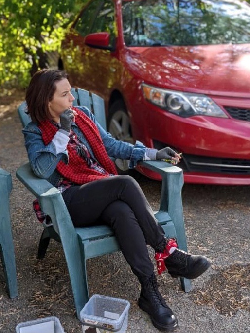 Claire, dressed as John Bender from The Breakfast Club, lounges in an Adirondack chair outside. She has a sucker in her mouth and joint in her hand. 