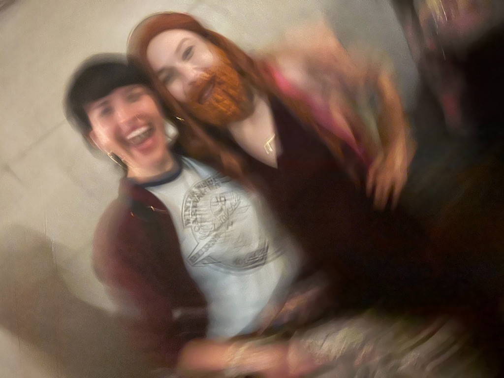 A blurry photo of Claire, dressed as Gemma, and Emily Axford, smiling and laughing backstage after a NADDPOD show. 