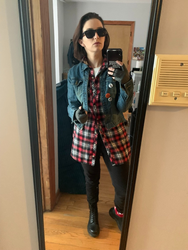 Claire, dressed as John Bender from The Breakfast Club, poses in a mirror selfie. She wears sunglasses and holds her phone visibly for the shot. 