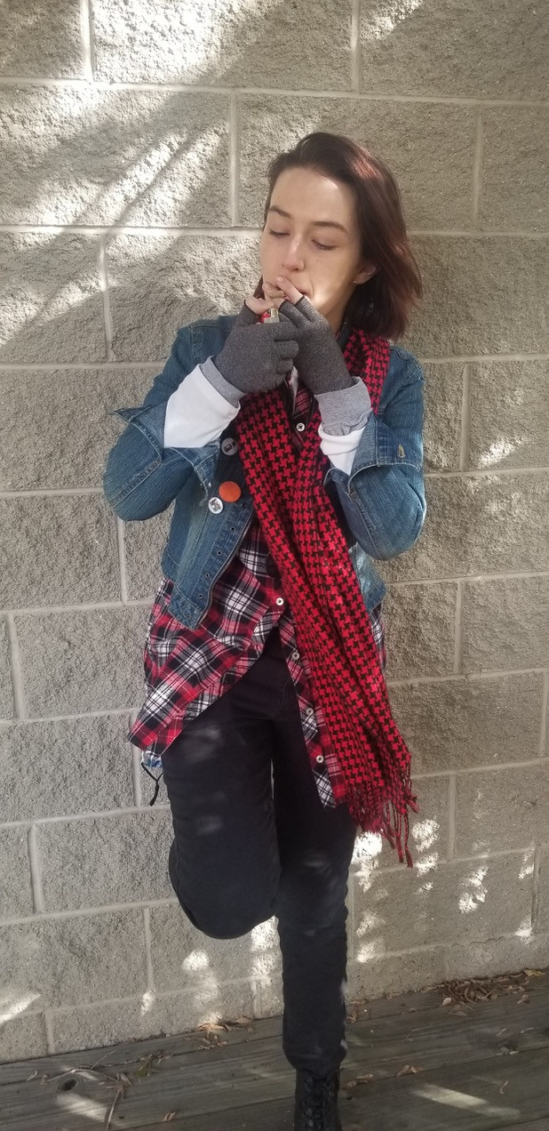 Claire, dressed as John Bender from The Breakfast Club, leans against a brick wall, lighting a joint. There's a slight breeze and she looks very cool. 