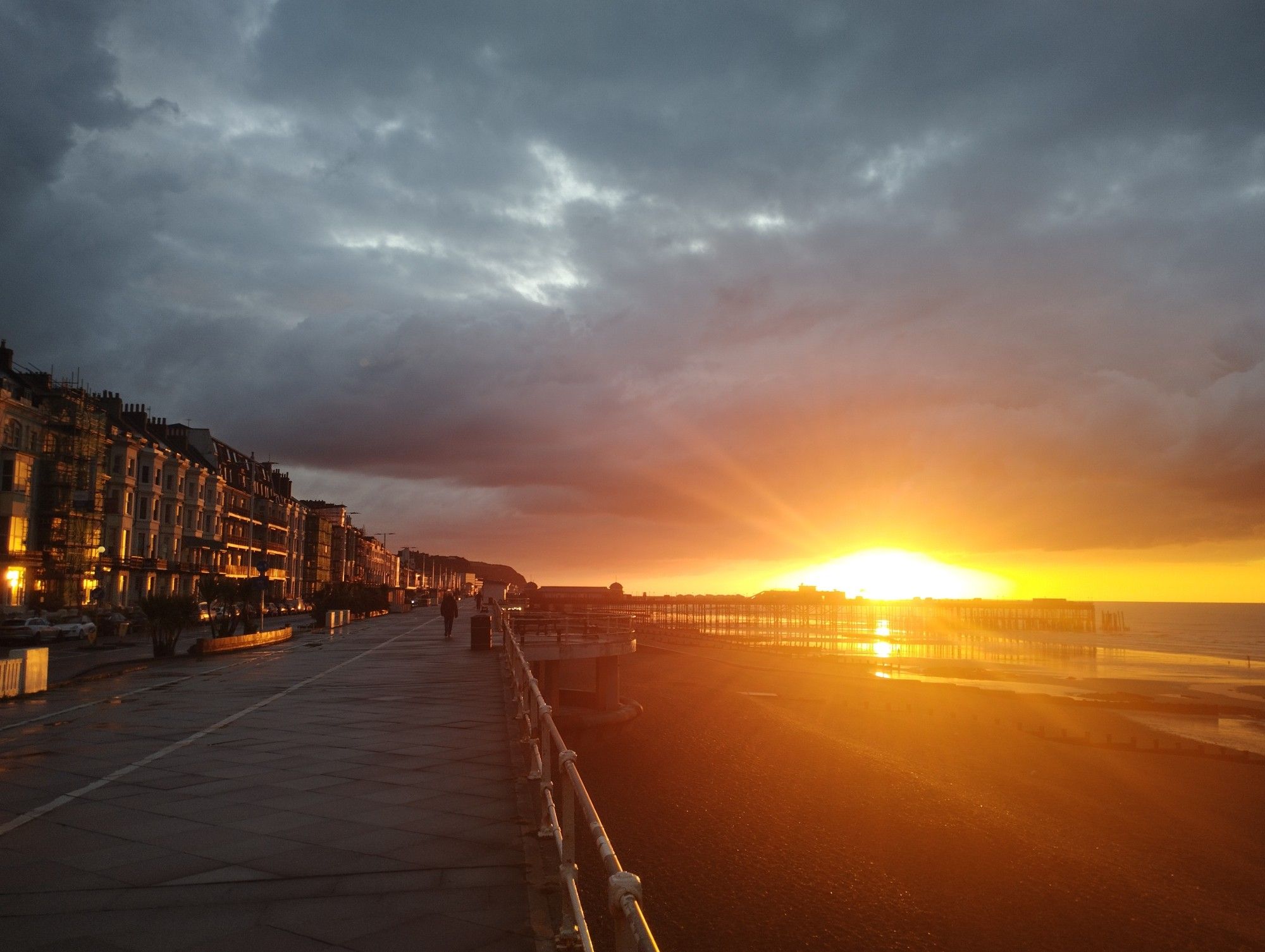 wide shot of the promenade and hastings pier, with dawn breaking over the pier. it looks like it's on fire