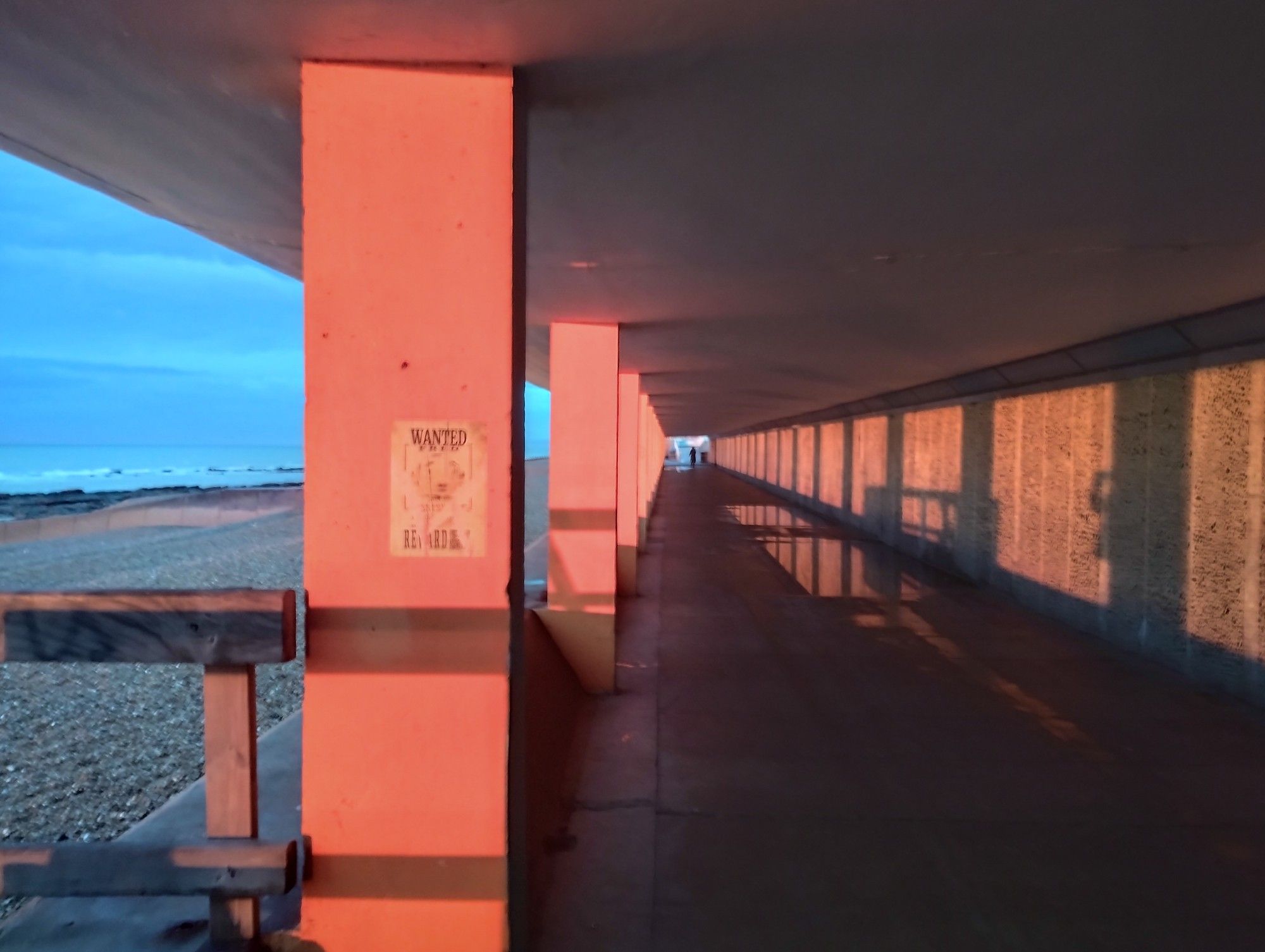 the view looking back down Bottle Alley, the underside of the promenade, which has concrete pillars every ten yards. everythin is either bright pink or shadow