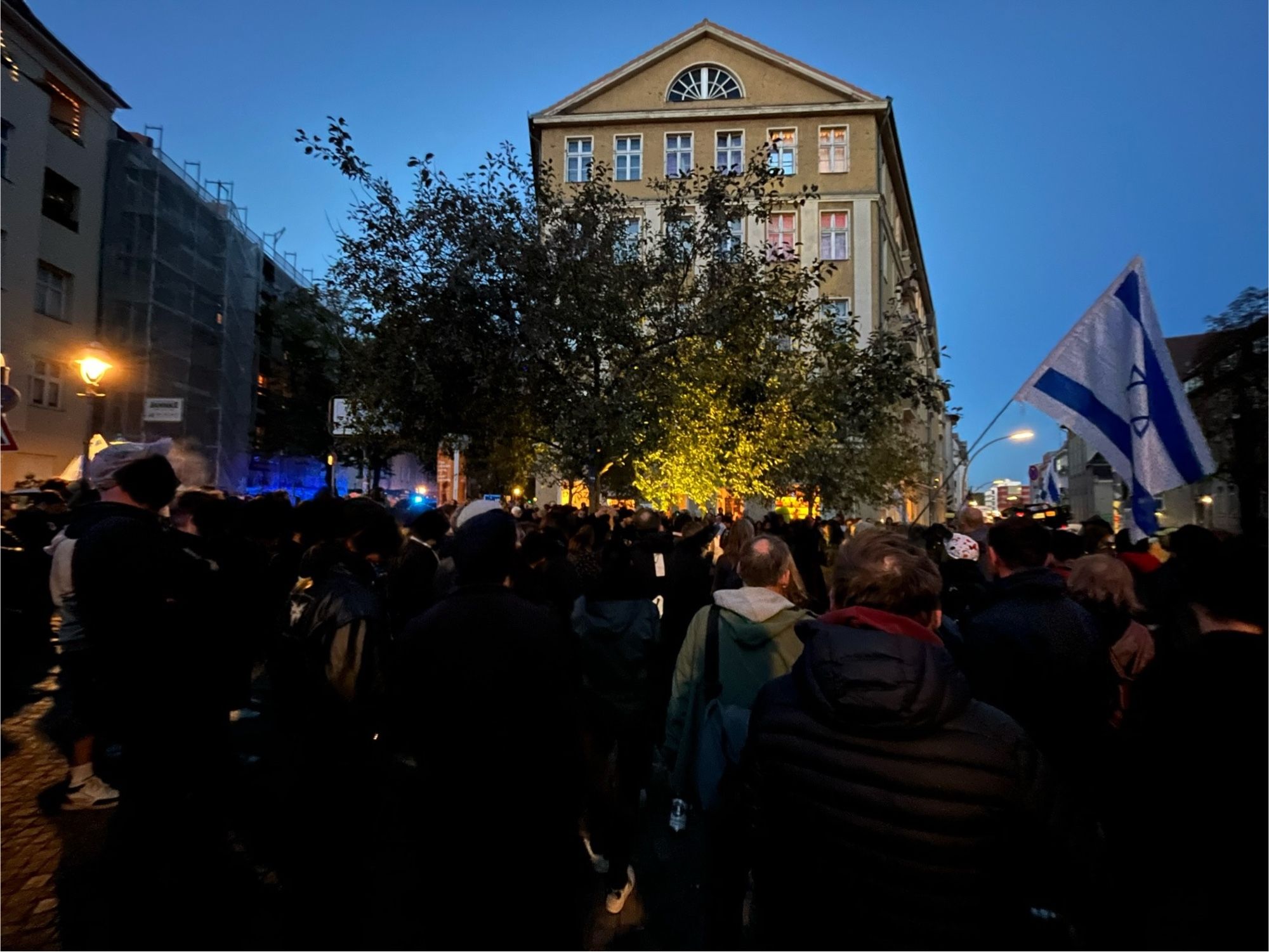 Eine Menschenmenge vor dem Baszjel. Es gibt eine Israelfahne. Überwiegend dunkel gekleidet, aber erkennbar eher 30+ als 20+
Im Hintergrund ist Blaulicht zu erkennen.