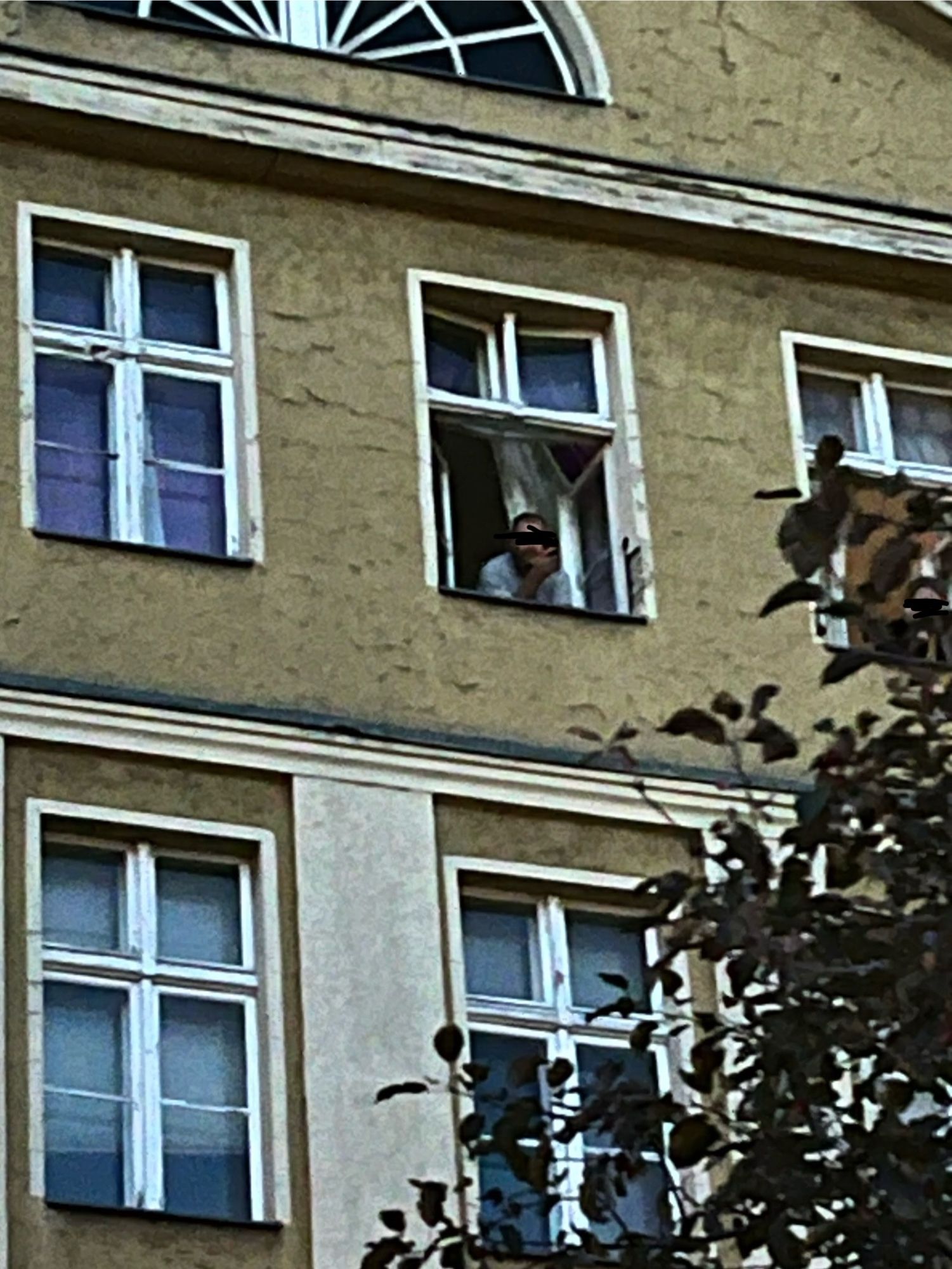 Ein Mann mit einem Schal mit Palästinaflagge schaut aus dem Haus Bajszel aus dem Fenster und filmt die Demonstration.