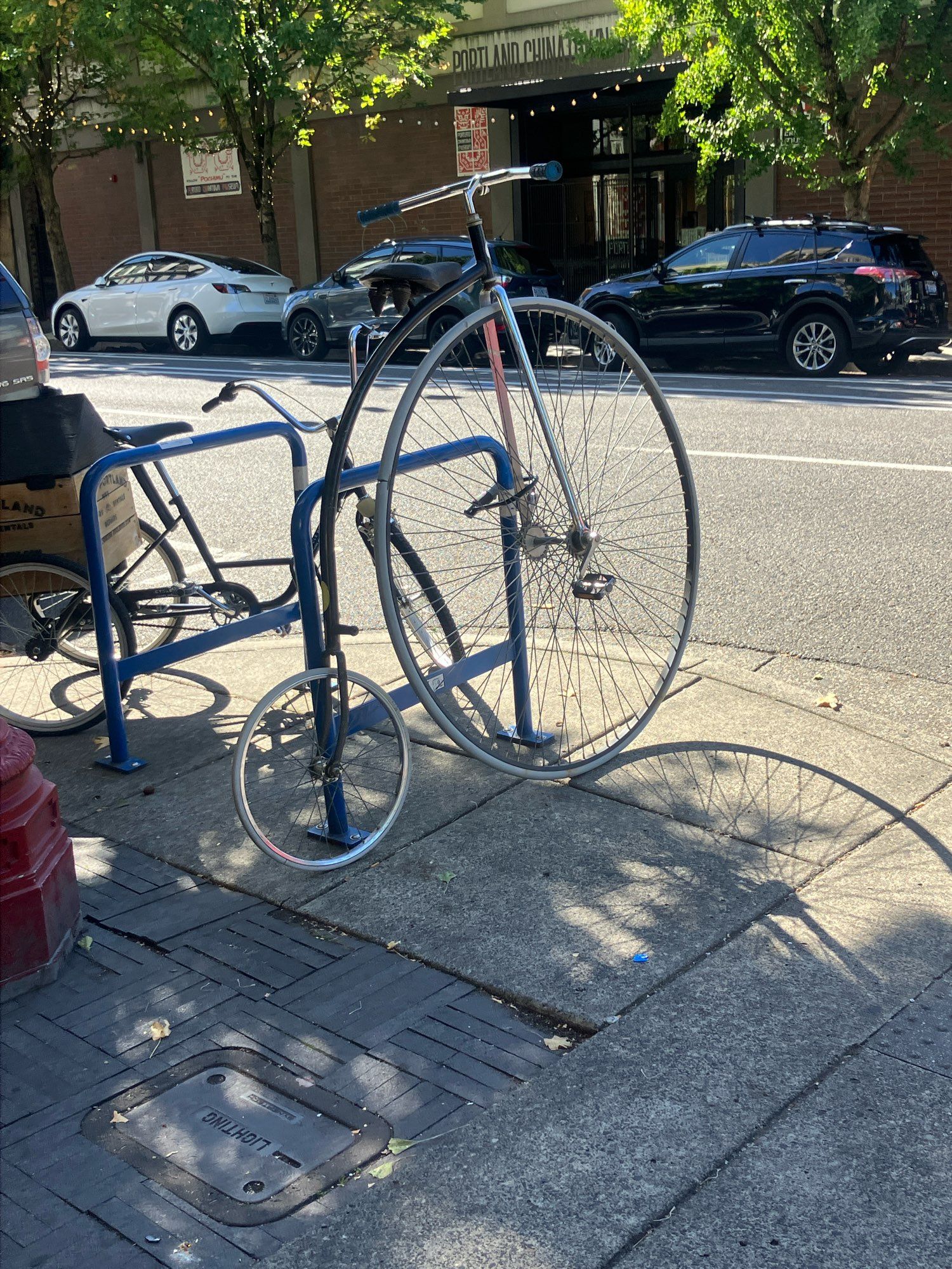 Bike with a large front wheel and a small back wheel with a long,arched body. The bike is tied to a bike rack on a street corner.