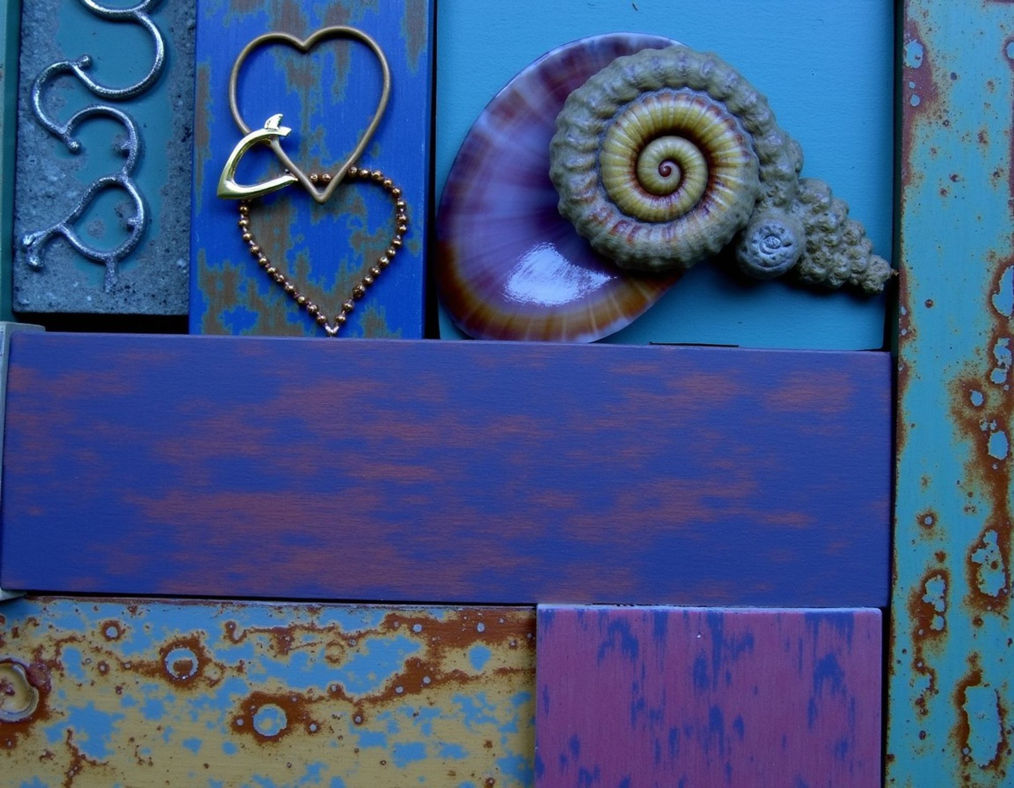 Underwater arrangement of seashells, hooks, and metal fishtail and heart shapes on corroded blue and purple metal panels.