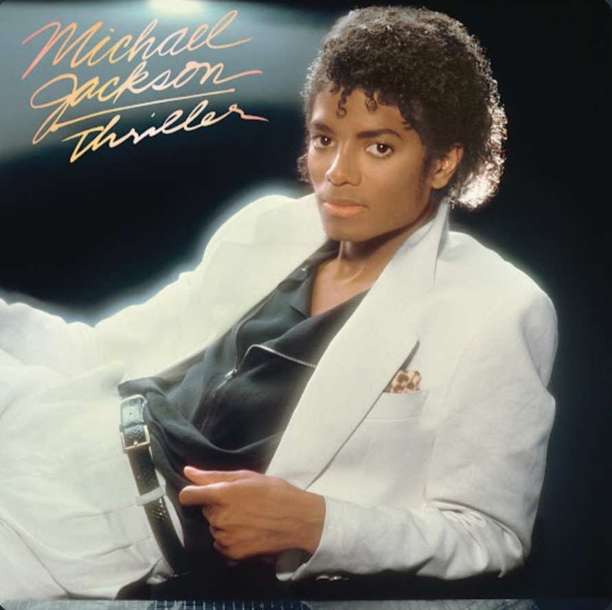 Michael Jackson wearing a white suit and pants, and a black dress shirt beneath. His pants fit up to the bottom of his torso. He looks at the camera.