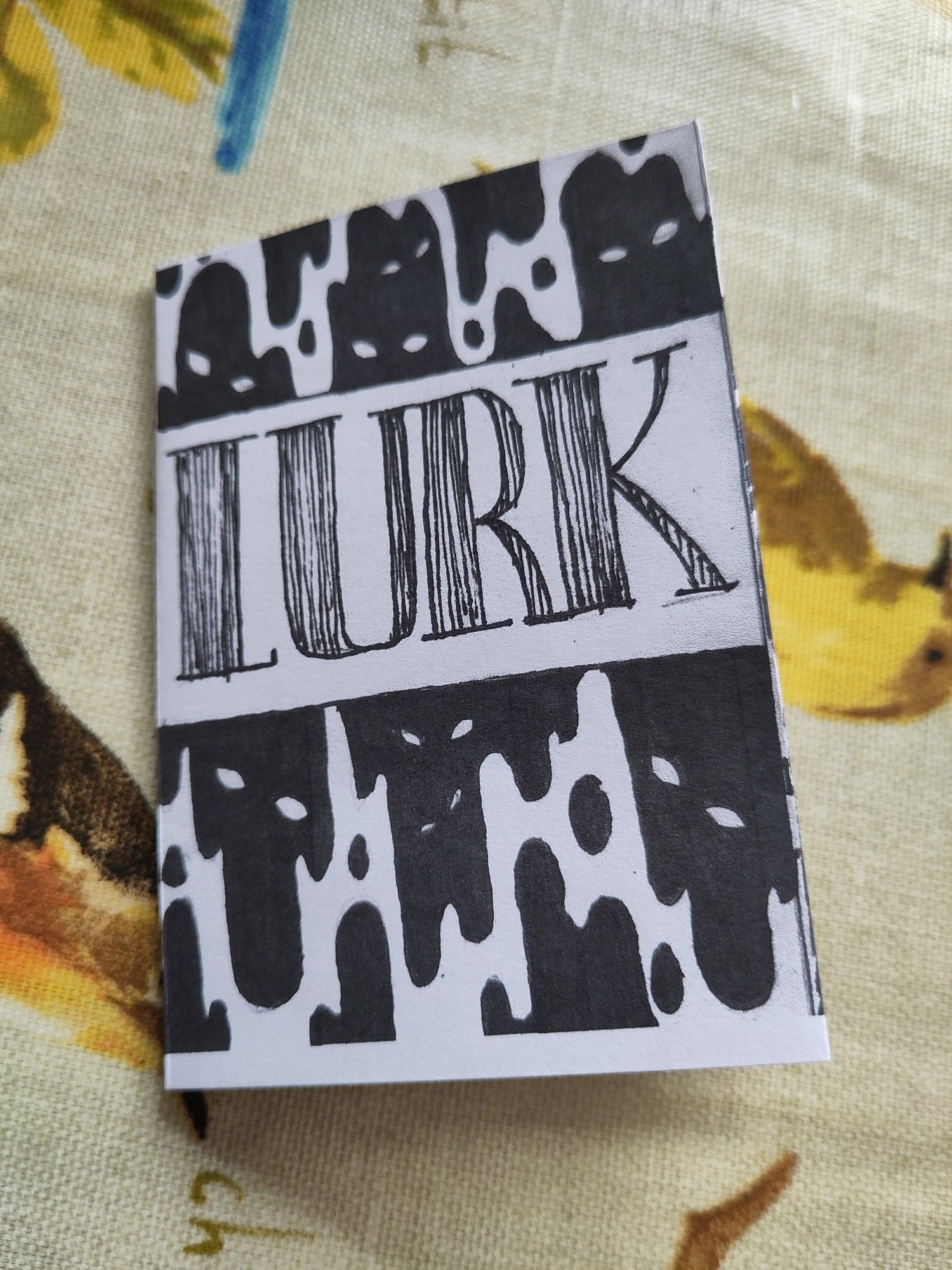 A mini zine, the title is Lurk and the imagery is black drips with eyes hidden in the shadows