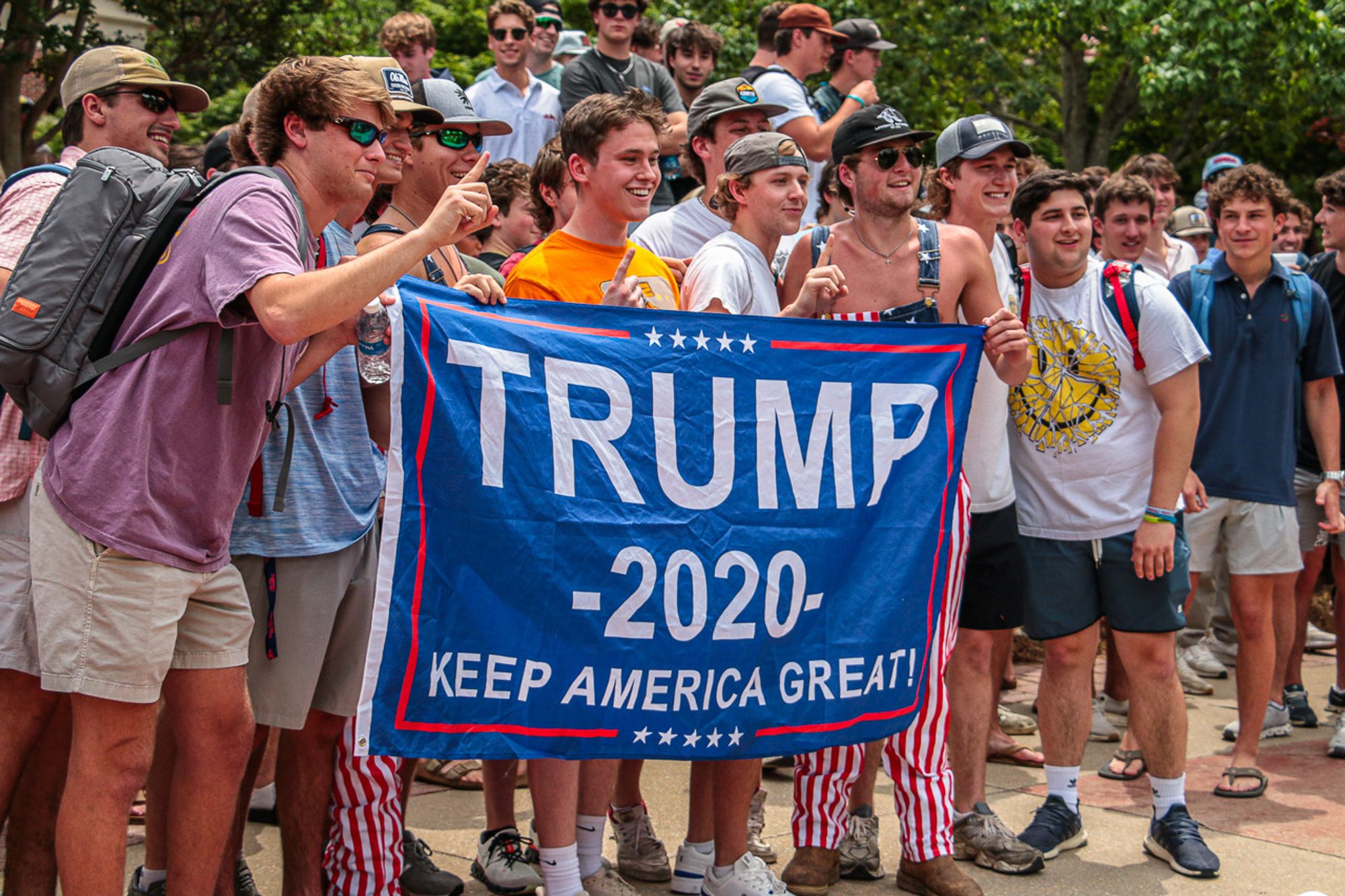 photo of a couple of dozen counter-demonstrators at UMiss mocking a pro-Palestinian demonstration. Many are wearing baseball caps and sunglasses and two have stars and stripes overalls. The ones in front are holding up a TRUMP 2020 flag. All are white, all male, and could fairly be described as chuds. Photo from https://thedmonline.com/may-2nd-pro-palestine-protest/