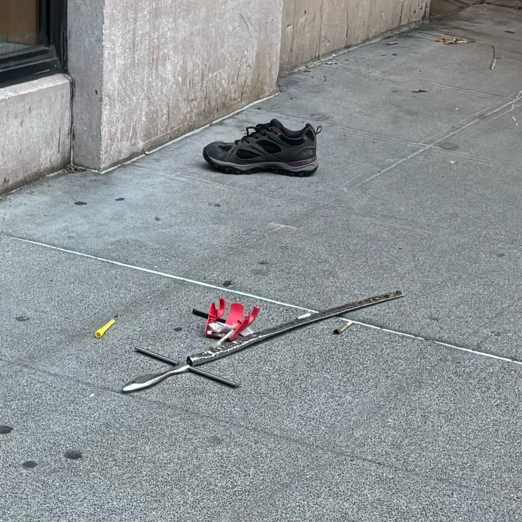 A makeshift sword laying on the street surrounded by some light trash and a half smoked joint. A few feet away is a single black sneaker.