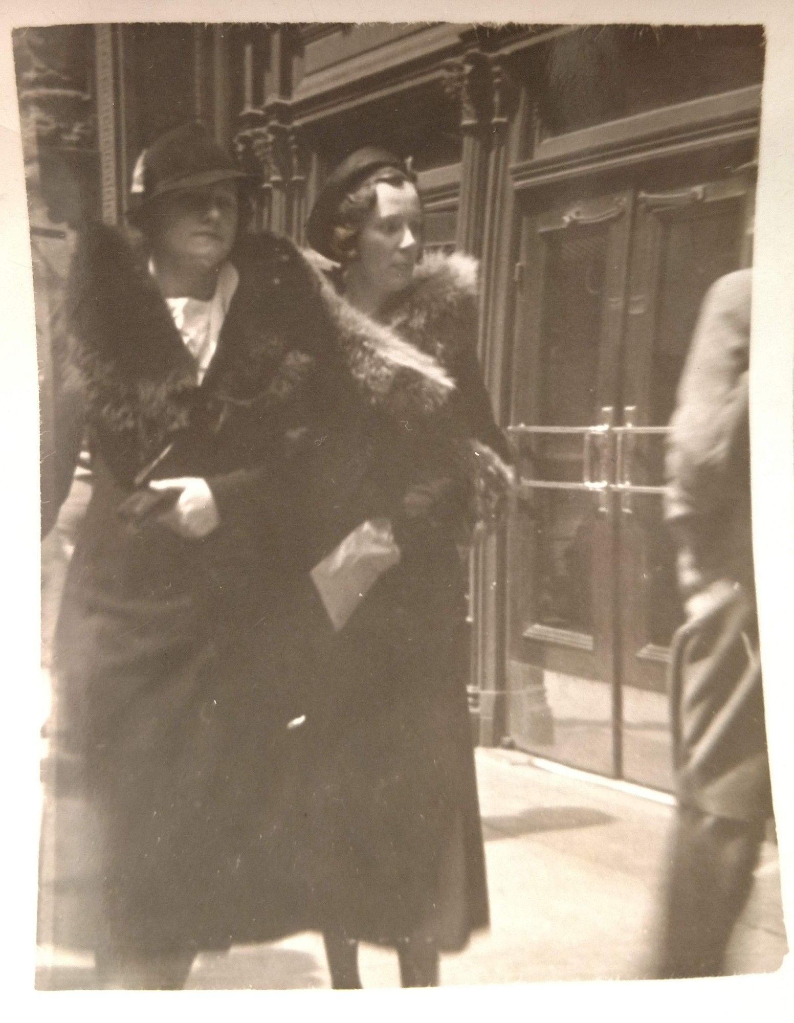 Black and white photo of two young women in hats and long coats with fur collars walking down a street. My grandma is at left, looking gorgeous & self-assured in a trilby-style hat. Her friend on the right wears more of a cloche and has serious Kirsten Wiig energy.