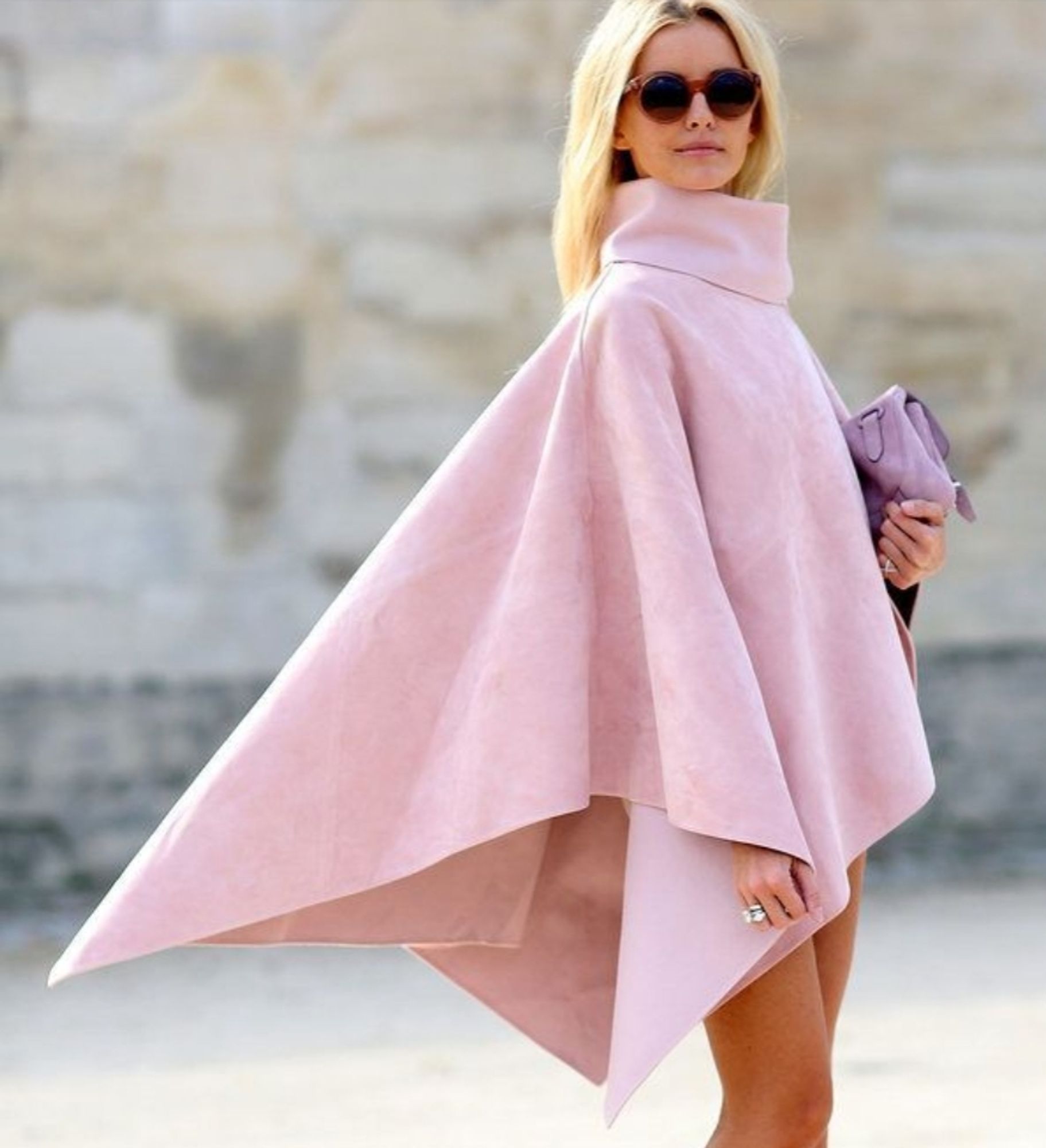 A model? or influencer? who is skinny, white, and blonde, wears sunglasses and carries a tiny purple clutch in a desperate effort to distract from the fact that her pink poncho with cowl neck is clearly a knock-off copy of the pink Nubbin no-chew cape