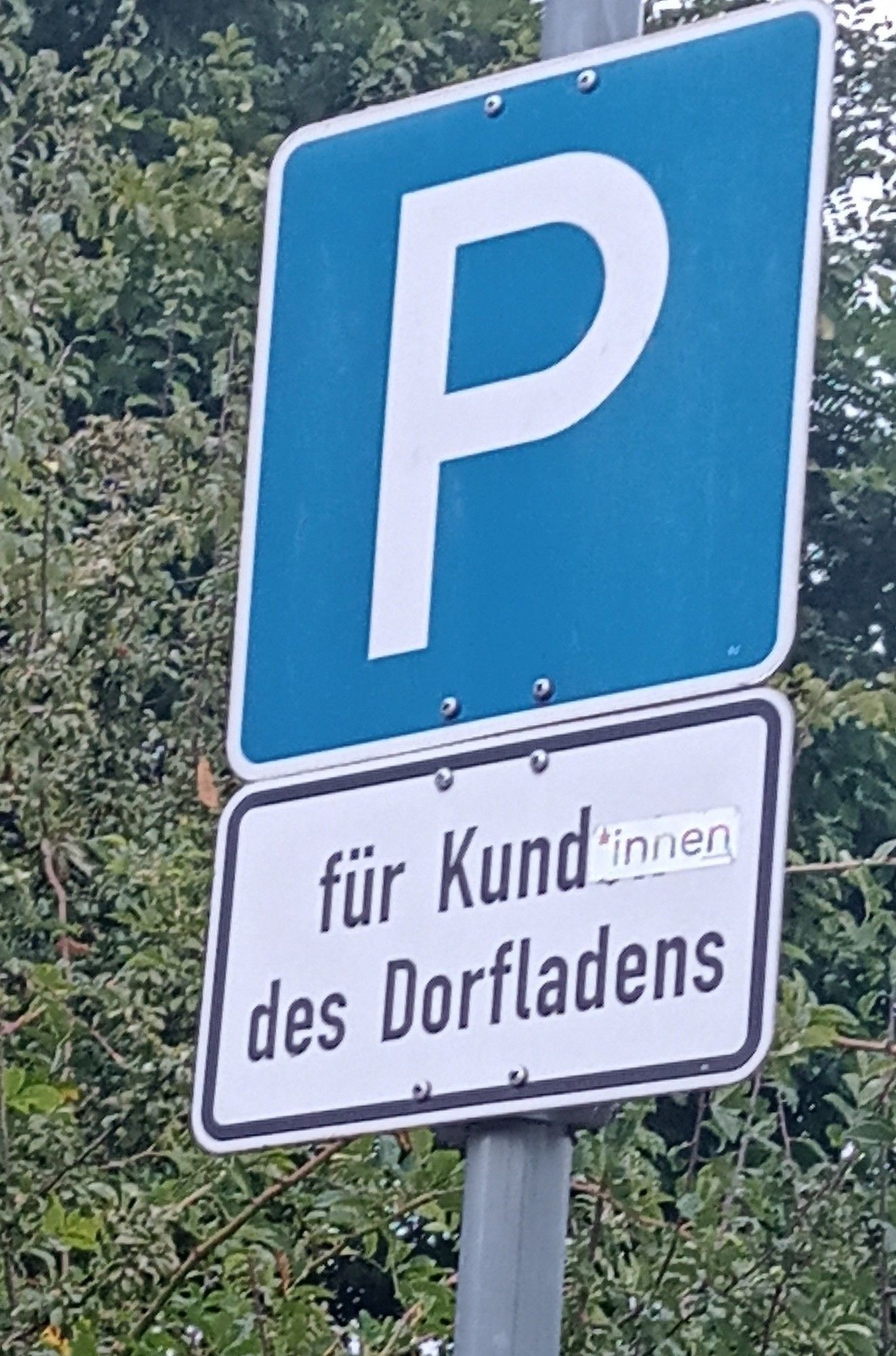 Parkplatz Schild "nur für Kund*innen des Dorfladens" das "en" in Kunden wurde mit "*innen" überklebt.