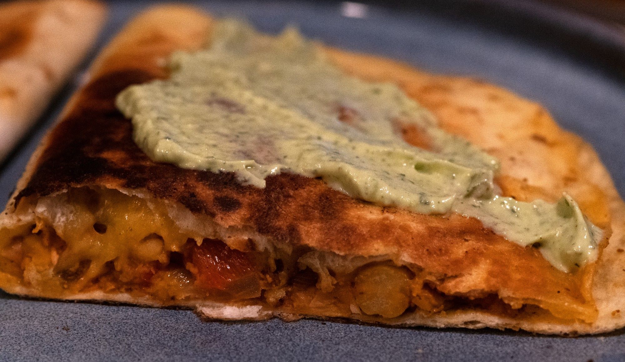 A toasted tortilla filled with chickpeas, veg and melted cheese, topped with a green sauce