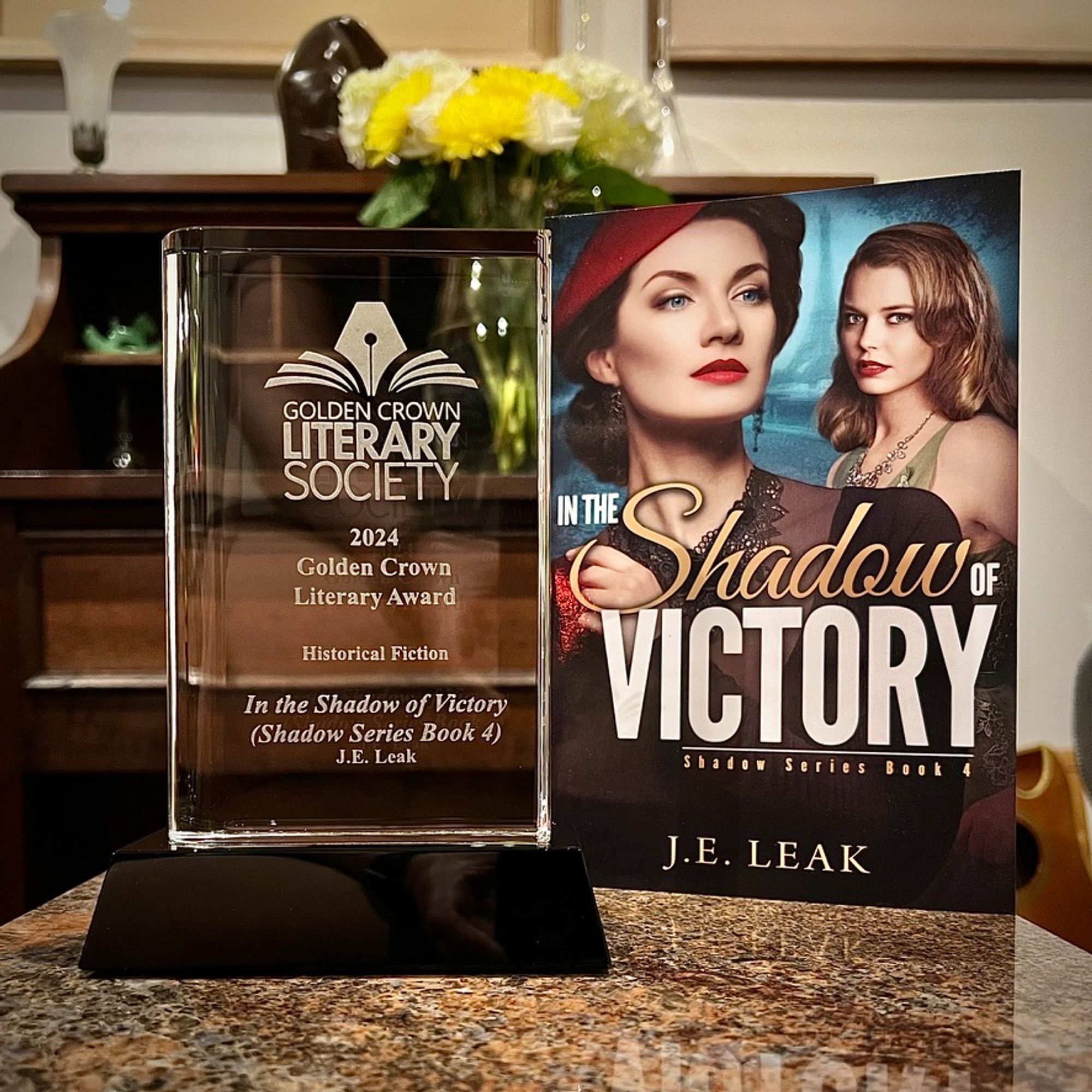 2024 Golden Crown Literary Award on a granite table top along with the winning book In the Shadow of Victory (Shadow Series Book 4) by J.E. Leak