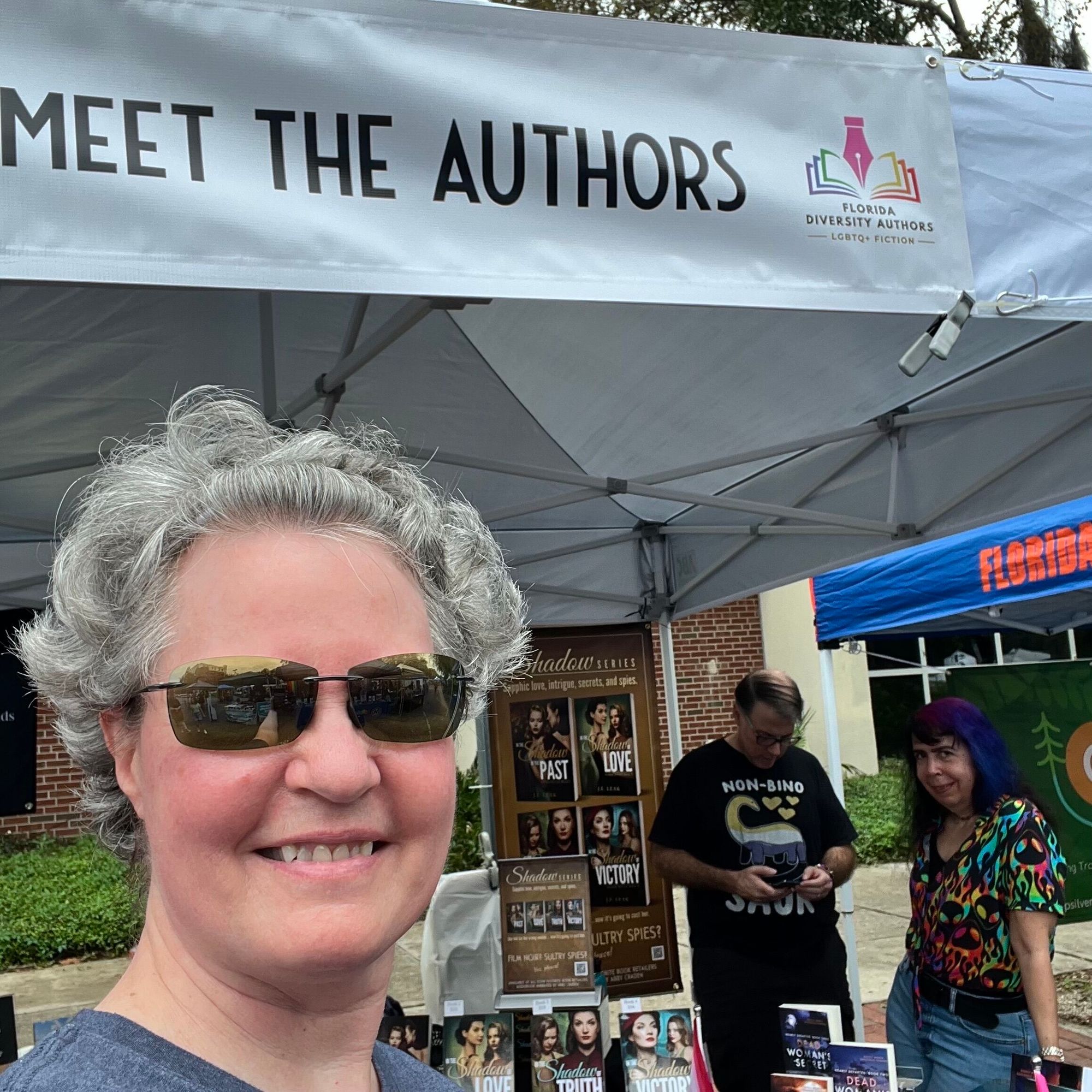 Author with book booth at Pride festival. A banner reads Meet the Authors .