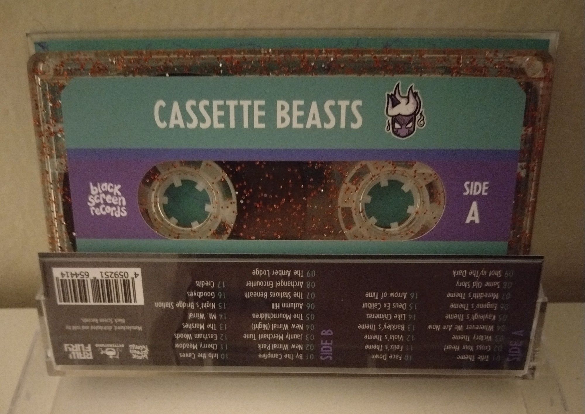 the cassette tape inside. it is clear, inlaid with glitter, and has a label on it reading "CASSETTE BEASTS" and "SIDE A".