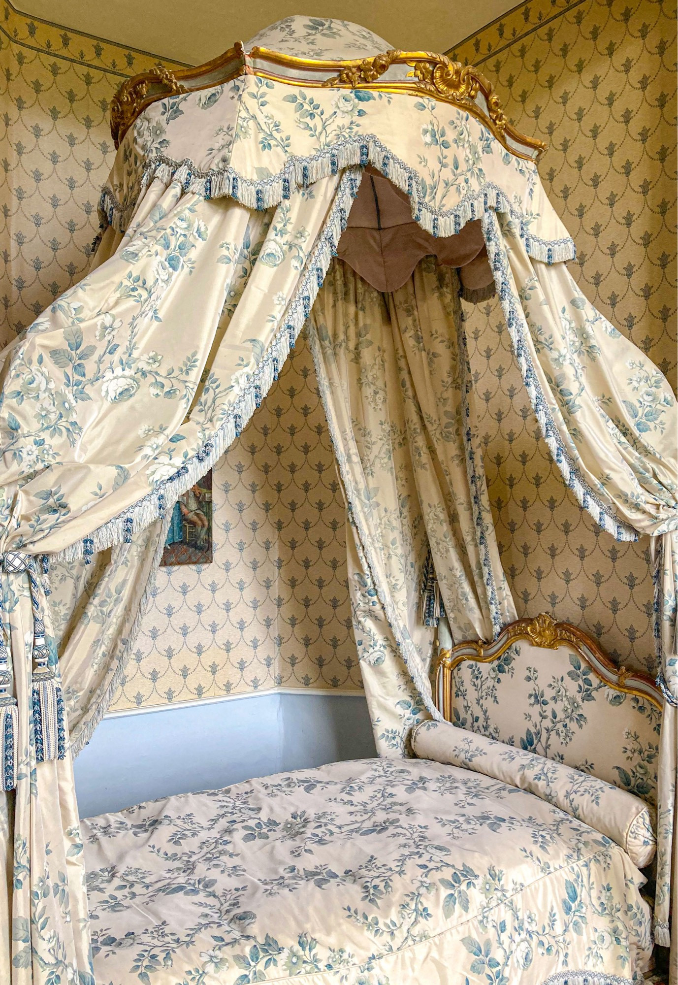 Ton in Ton Foto
Ein barockes Bett mit Baldachin. Beides mit blau-grünem floralen Muster auf hellgelben Grund. Die Tapete dahinter hat ein schlichtes blaues geometrisches Muster ebenfalls auf hellgelbem Grund.