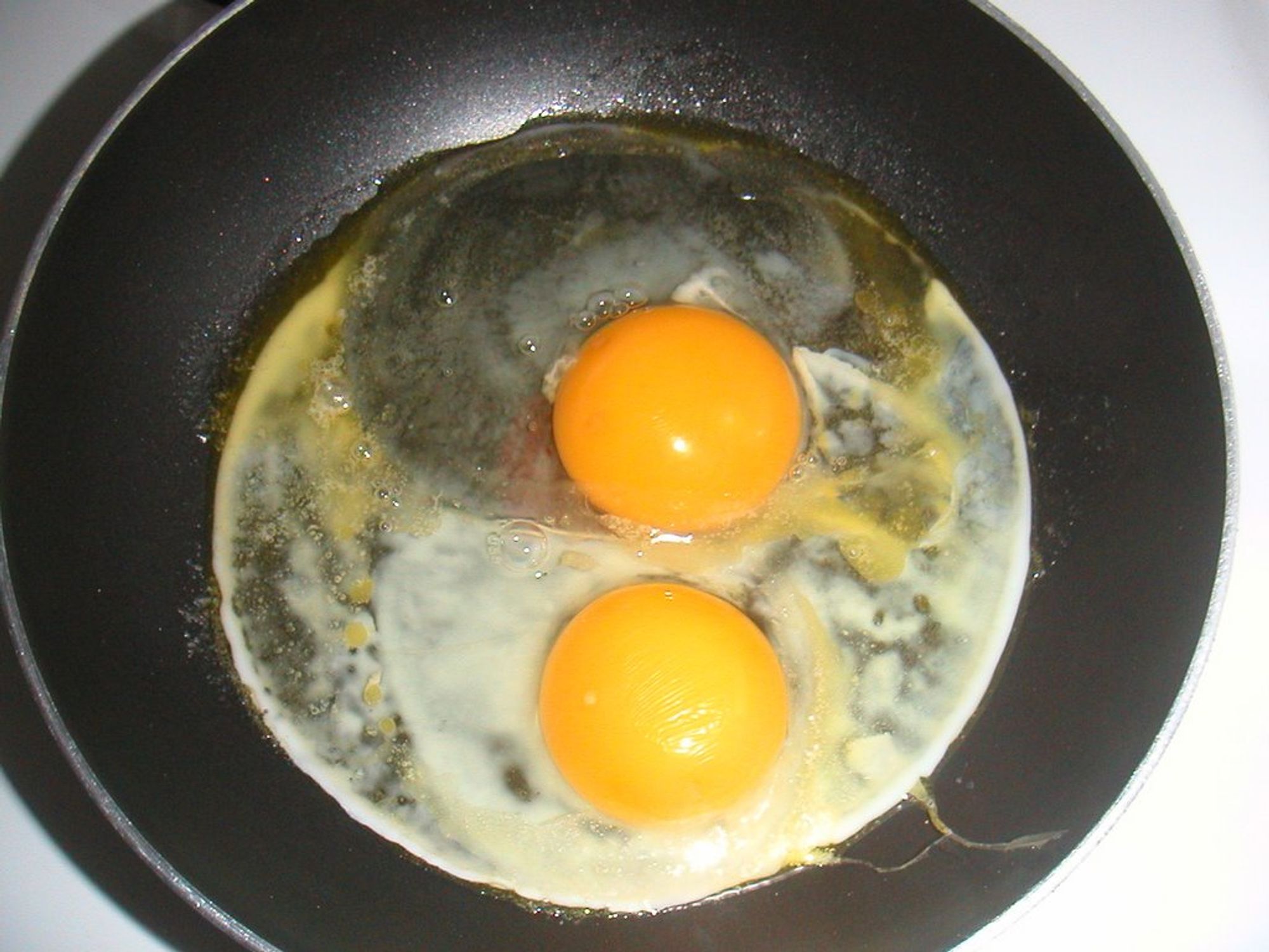 frying pan with two eggs, sunny side up, just beginning to cook