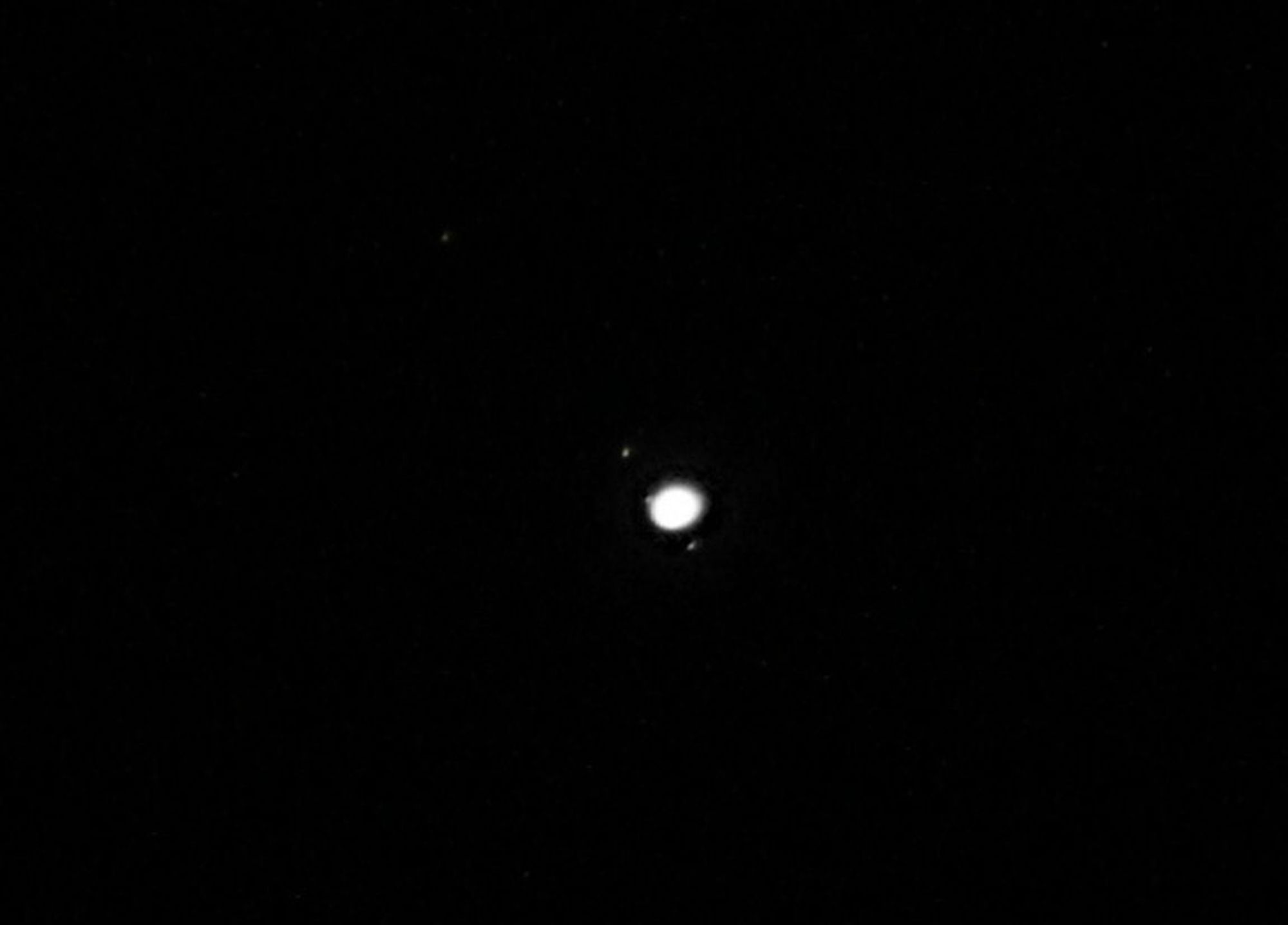 Planet Jupiter at centre. Moons Callisto and Io to its left. Moon Ganymede close to the planet. Moon Europa below Jupiter.