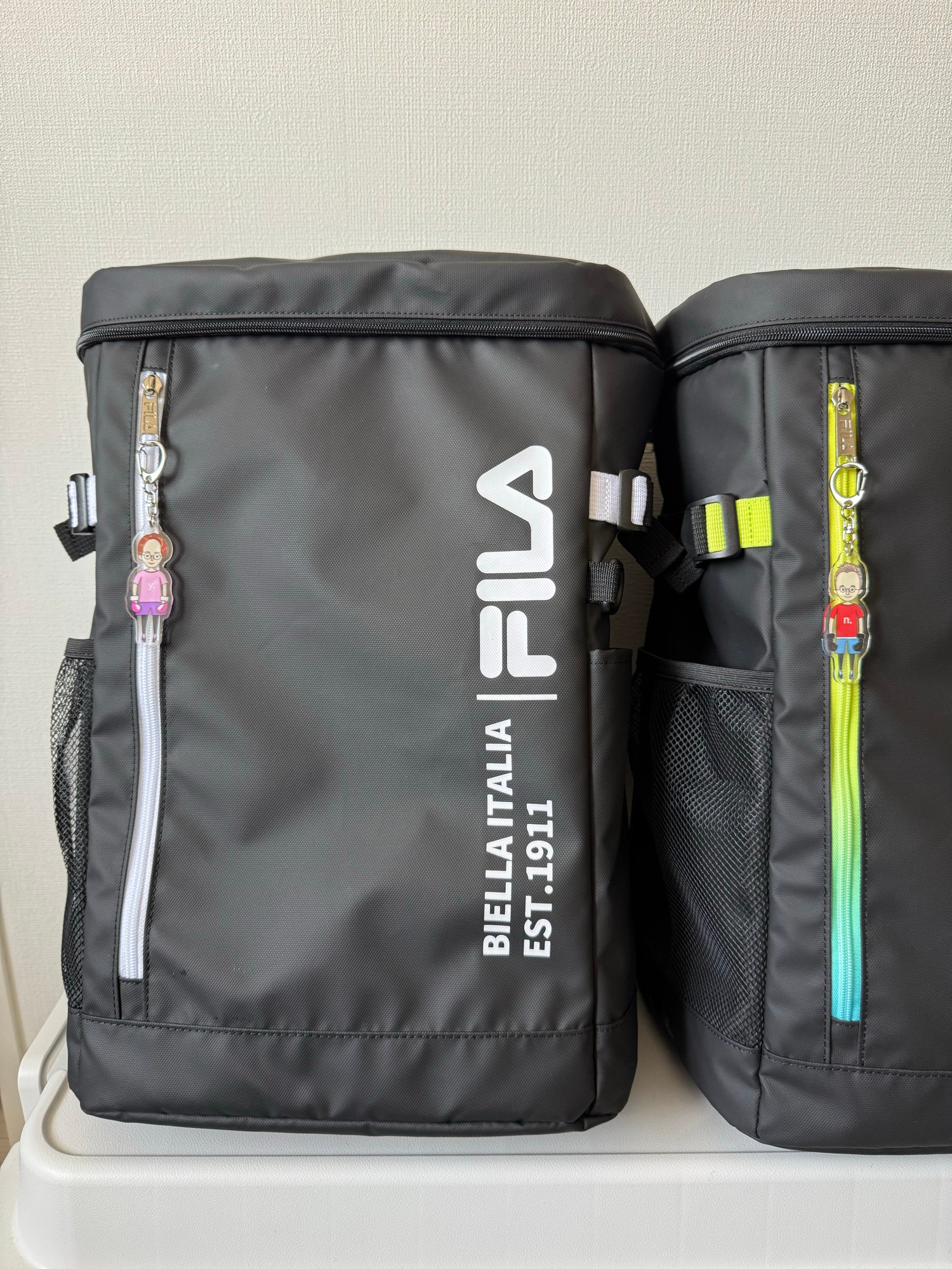Two key rings with illustrations of a male and a female character in kickboxing sports gear, attached to zippers on two sports bags.