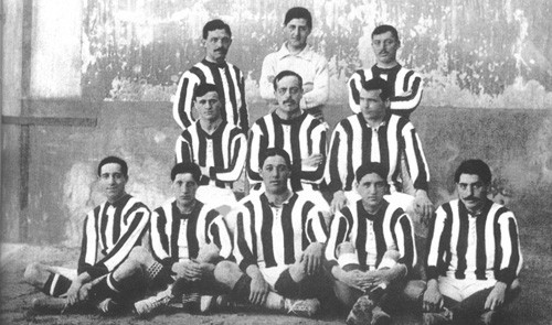 6.2 - Foto do elenco do Athletic de Madrid de 1911. As peças anteriores eram confeccionadas com um tecido muito áspero e desconfortável, que também desbotava bastante. Com as novas cores, porém, os madrilenhos resolveram adotar o azul em seus calções, diferente da cor preta do Athletic. No dia 22 de janeiro de 1911, o Athletic Club de Madrid disputou o seu primeiro jogo como equipa vermelha e branca, curiosamente diante do seu homólogo de Bilbao.