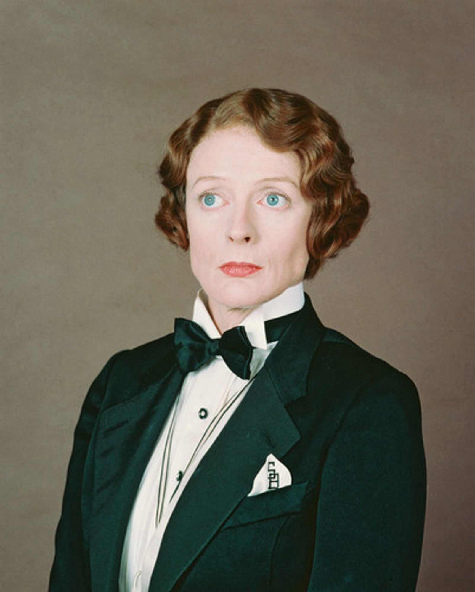 Dame Maggie Smith, in a black tuxedo jacket with black bow tie, with cropped red wavy hair