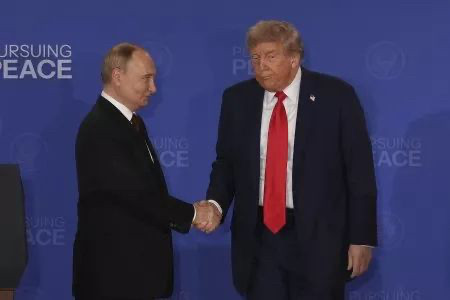Trump looking like an oaf shaking Putin's hand; Putin with an evil grin.