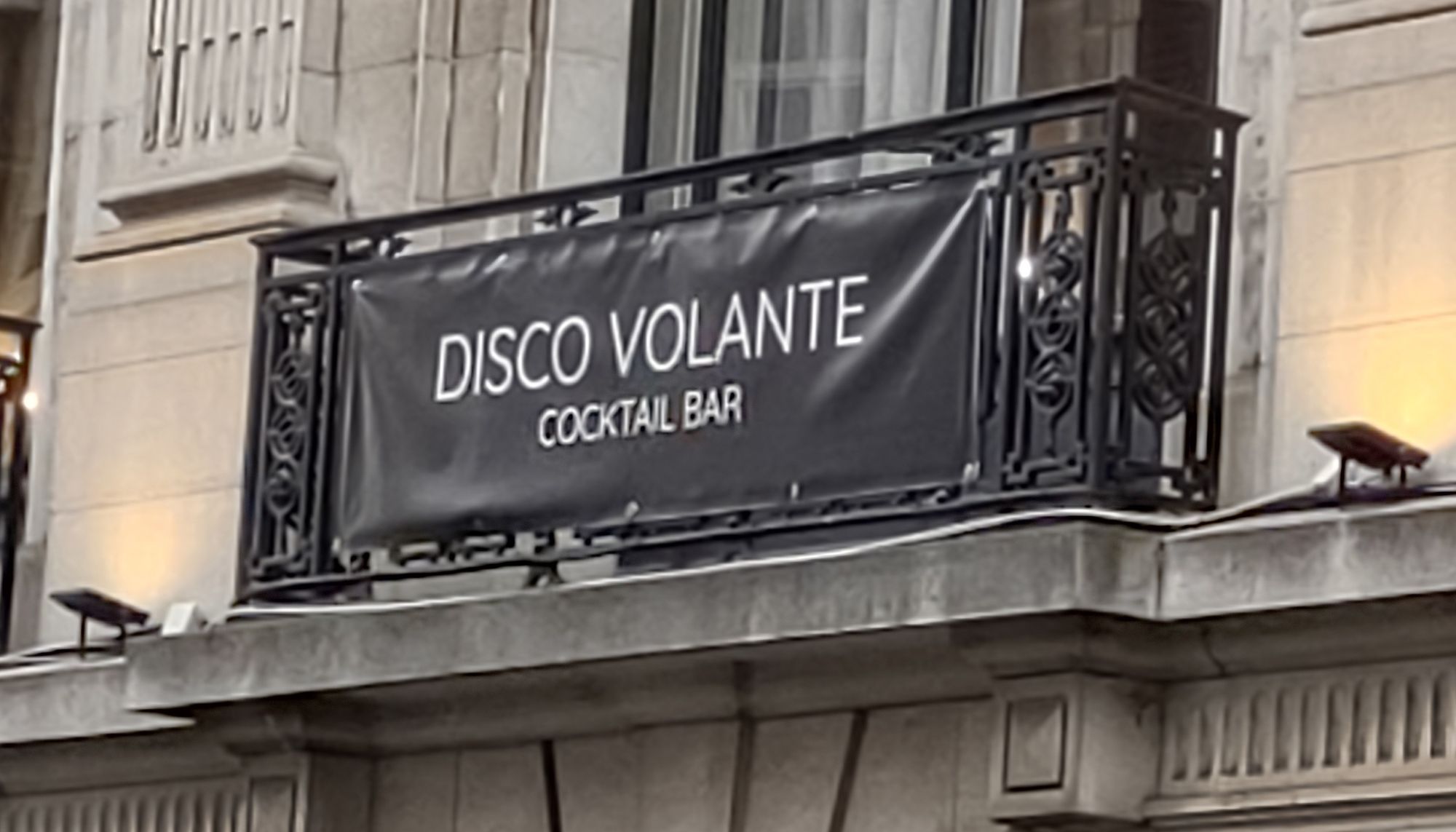 A black vinyl sign reading Disco Volante Cocktail Bar ( in white capitals) attached to the first floor balcony of the cocktail bar.