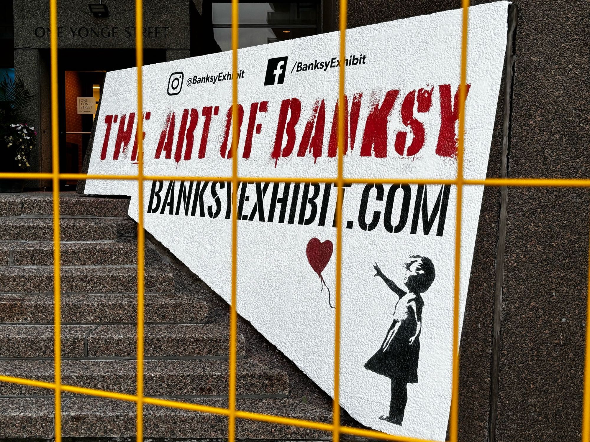 Street art ad for Banksy exhibit through construction fence