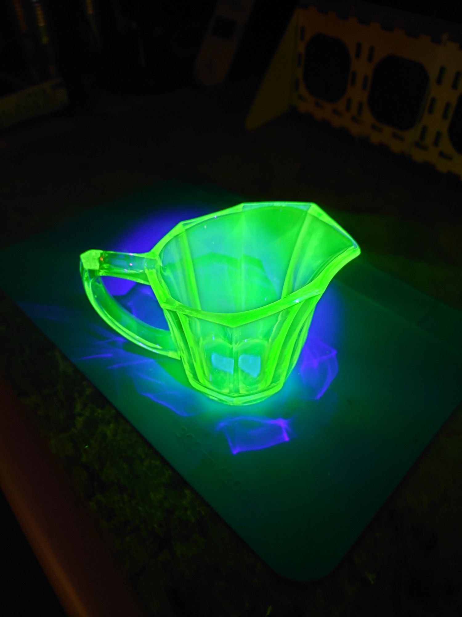 A picture of an uranium glass pitcher under UV light, glowing brightly.