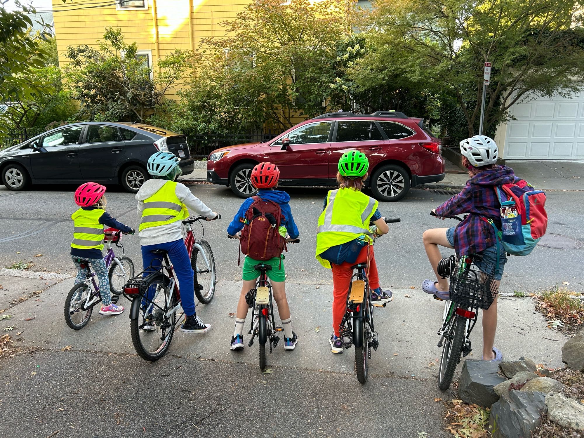 Five kids ages 5-13 perched on their own bikes at the edge of a city road.