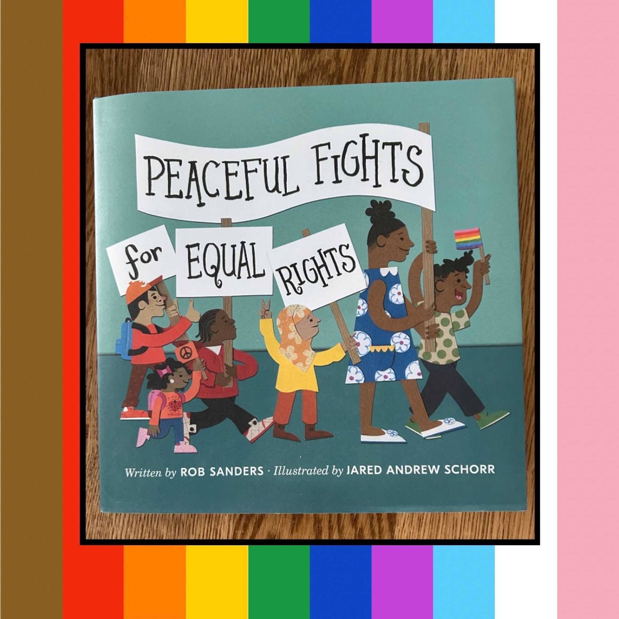 Rainbow striped graphic with a picture of a picture book cover on it. The picture book is PEACEFUL FIGHTS FOR EQUAL RIGHTS written by Rob Sanders and illustrated by Jared Andrew Schroeder. The book cover shows a group of people marching and holding signs with the title printed across several of the banners.