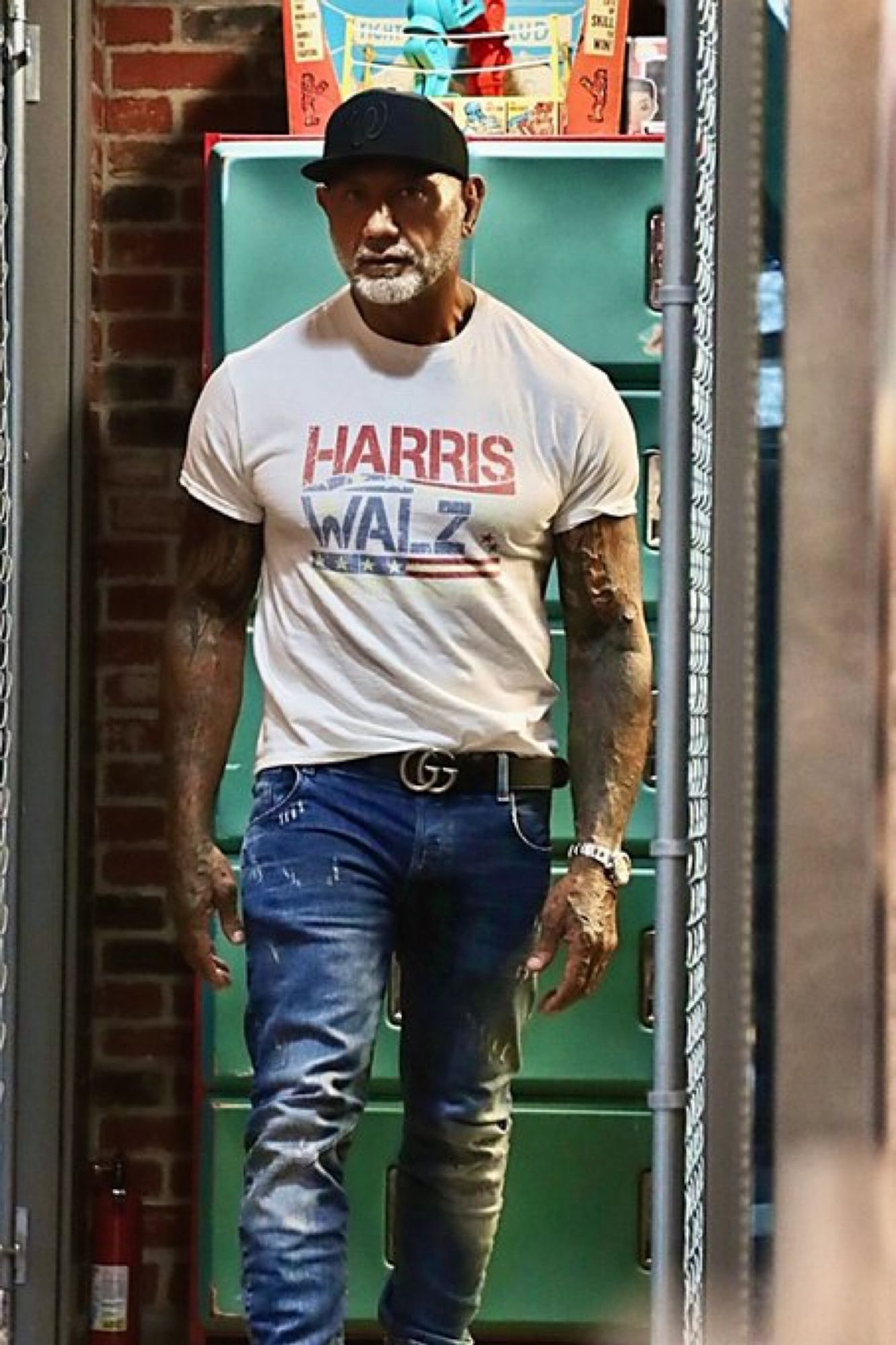 A muscled man wearing a white Harris-Walz t-shirt and jeans