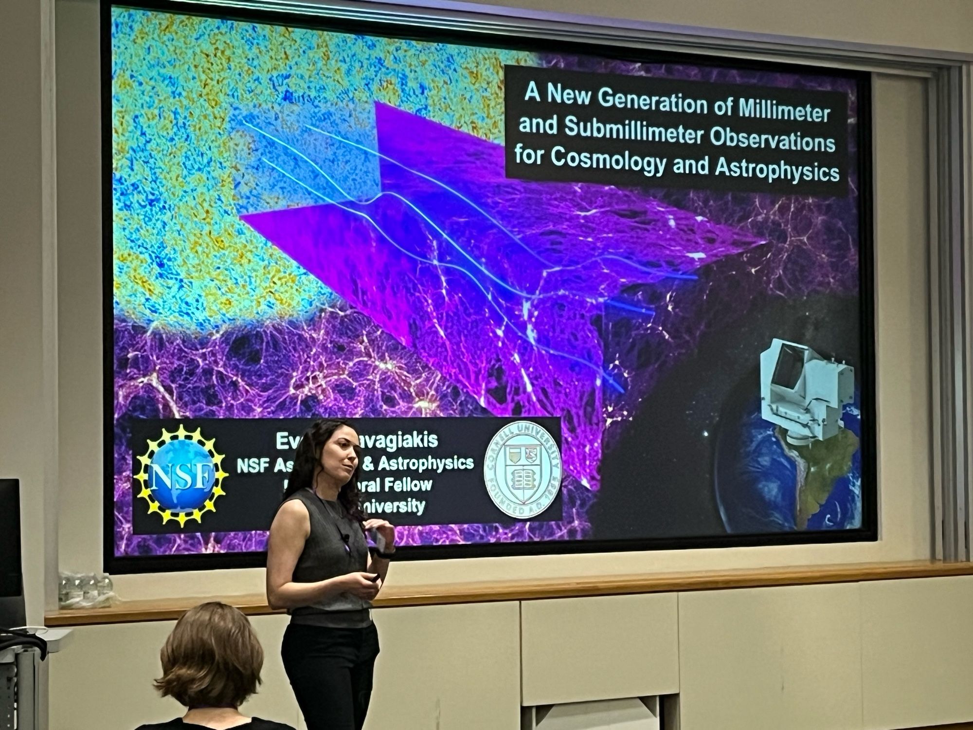 Dr. Eve Vavagiakas in front of her title slide depicting the cosmic microwave background and the path of photons through the intervening matter on their paths to our telescopes.