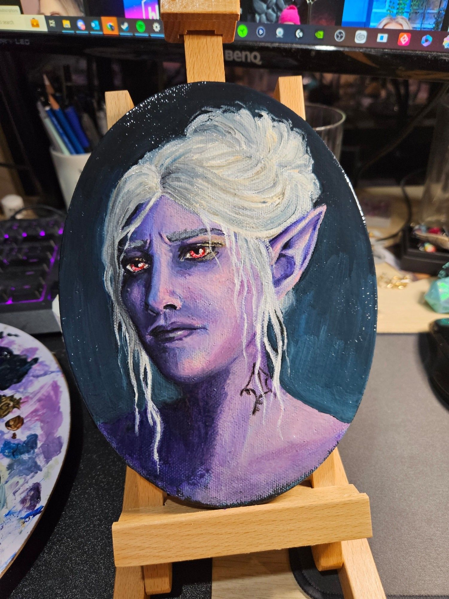 A painted oval canvas sitting on a small desktop easel. The painting depicts a lilac purple dark elf with white hair, looking away from the viewer at a 3/4 angle. She appears concerned or melancholic.